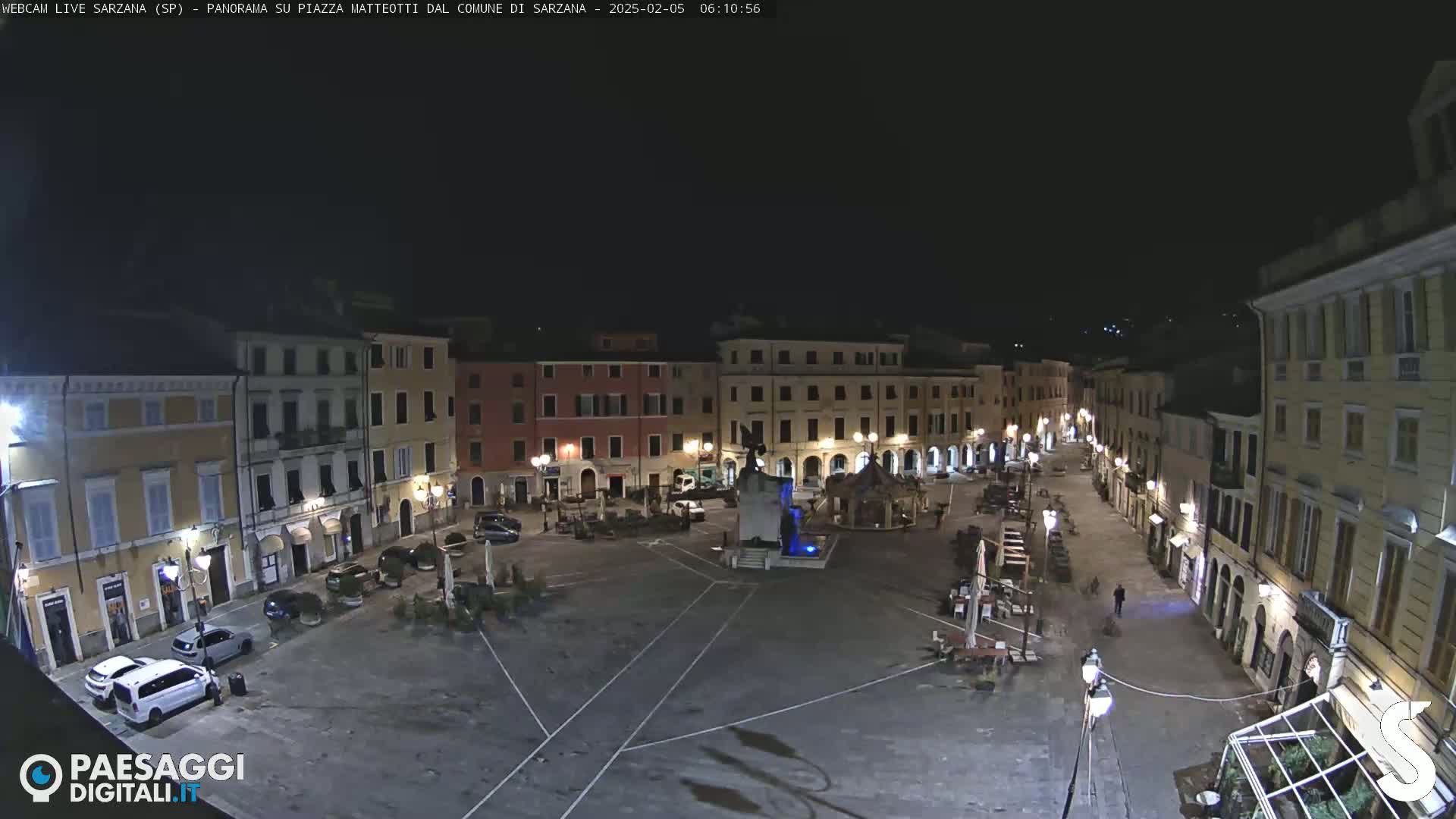 A nighttime view of a town square surrounded by buildings, illuminated by streetlights.