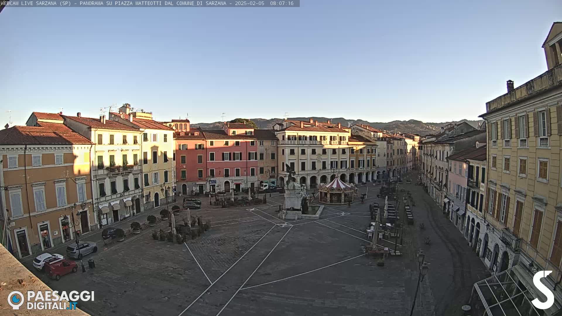 A mostly empty town square, surrounded by multi-story buildings, under a clear blue sky.