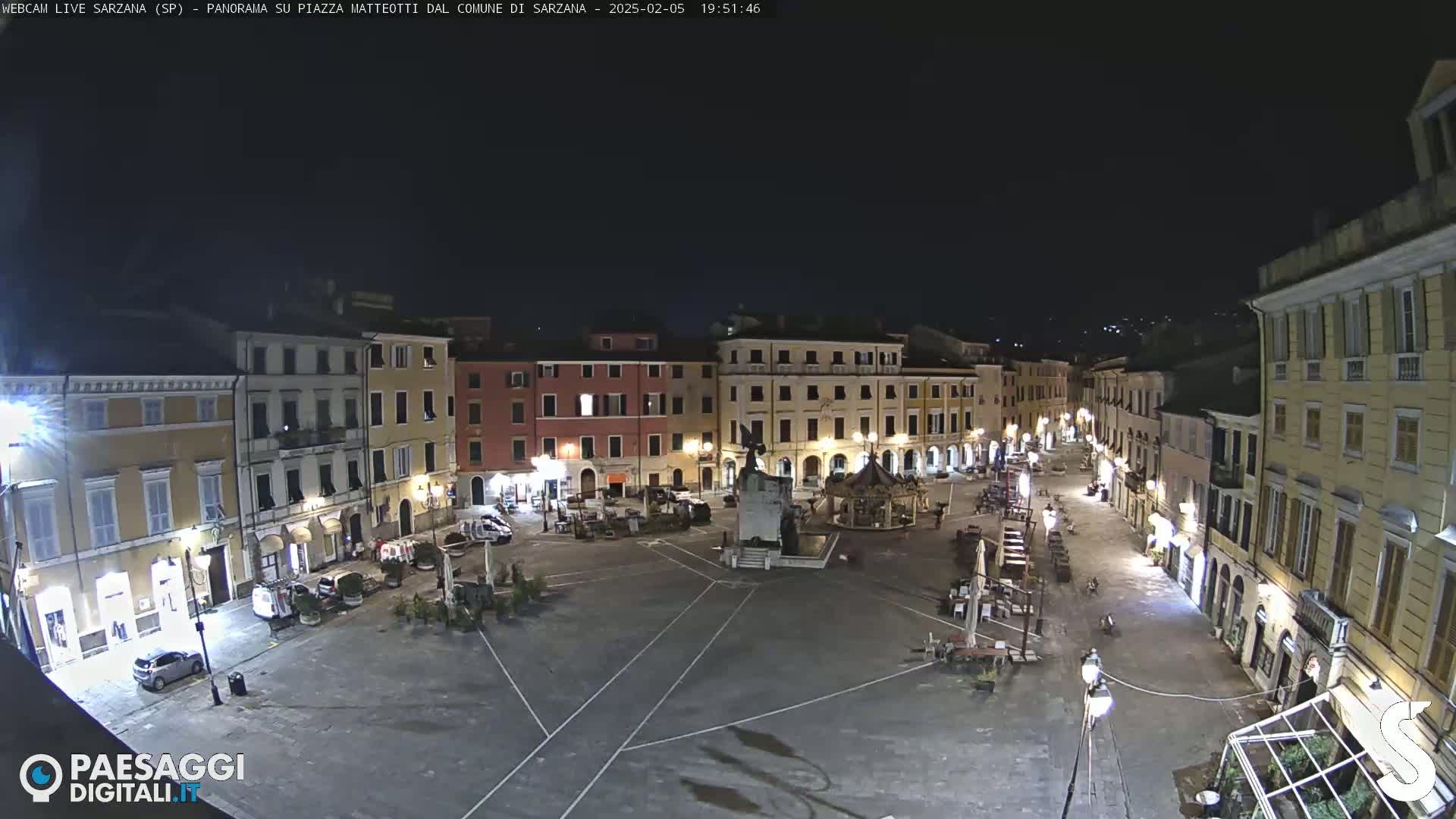 A nighttime, mostly empty town square is surrounded by illuminated buildings under a clear, dark sky.