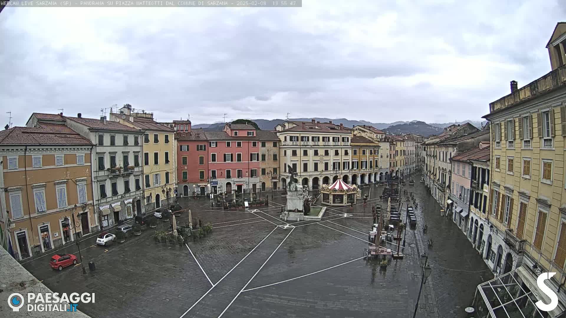 A wet town square in a European town, surrounded by multi-story buildings under an overcast sky.