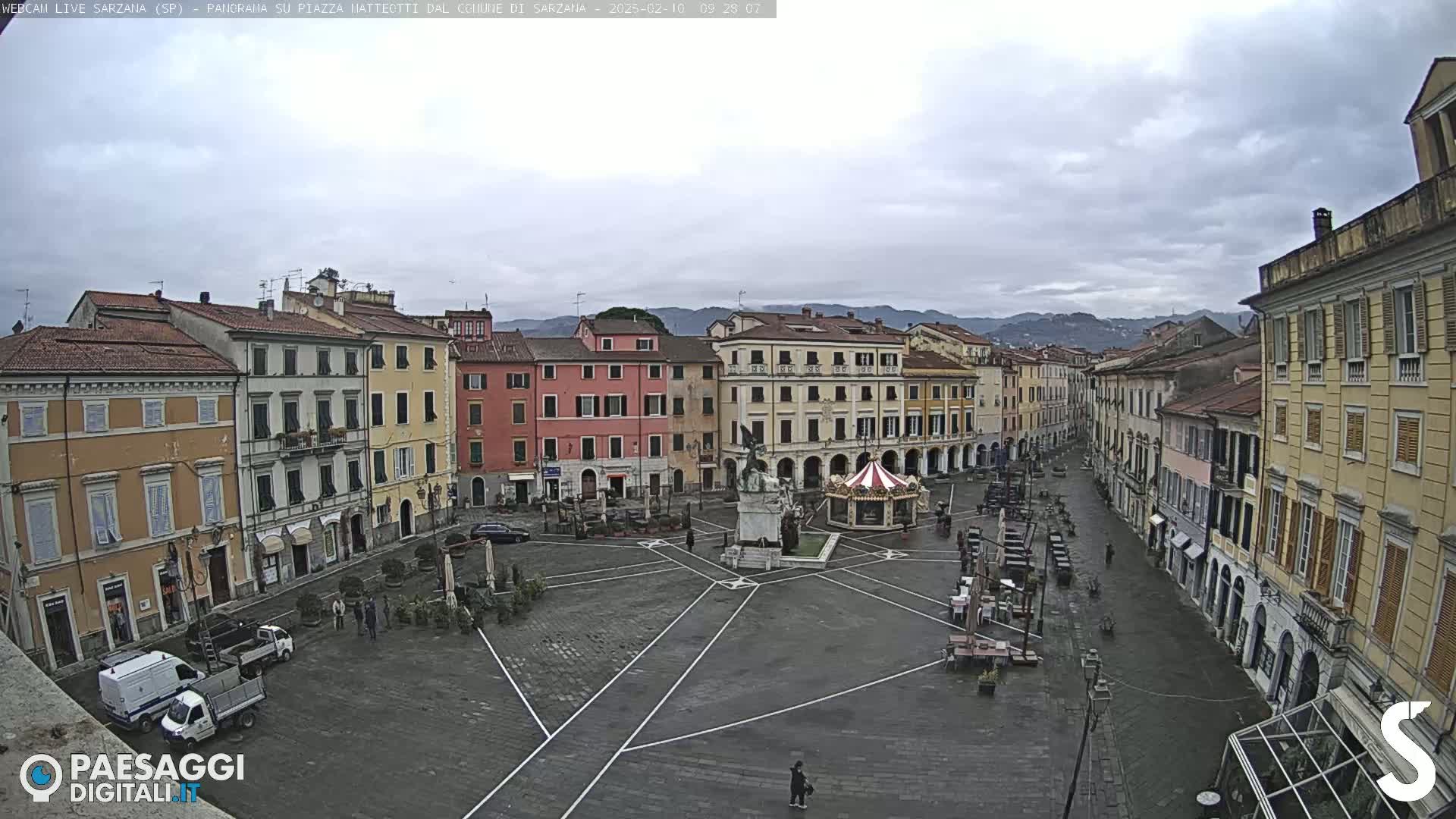 A mostly empty town square with surrounding buildings under an overcast sky.