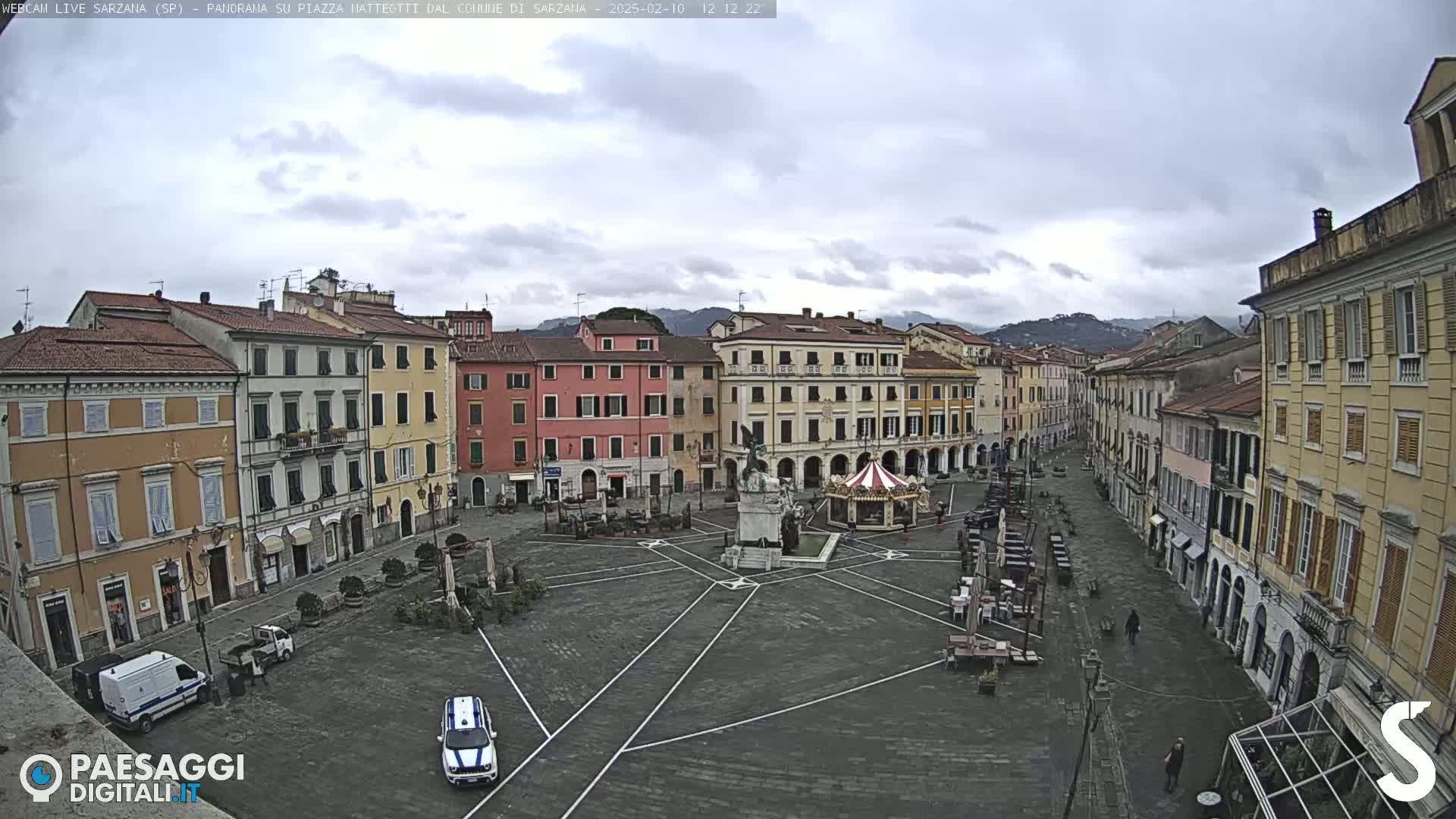A mostly empty town square with surrounding buildings under an overcast sky.