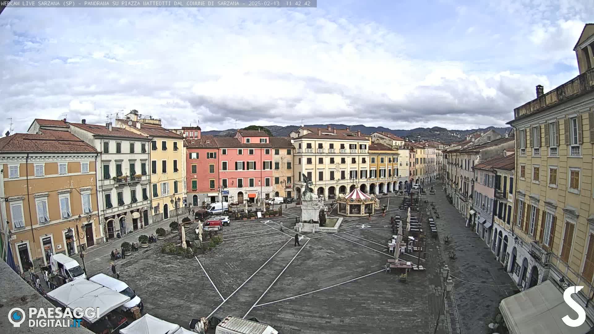 A large town square with multi-story buildings on all sides under a cloudy sky.