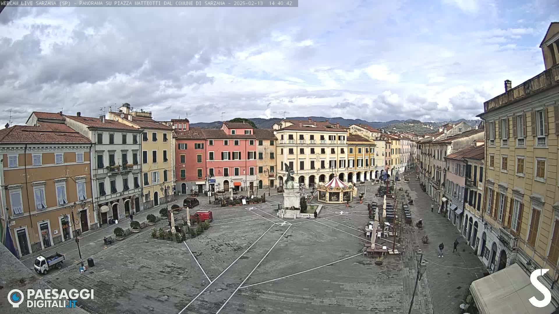 A mostly empty town square with surrounding buildings, under a partly cloudy sky.