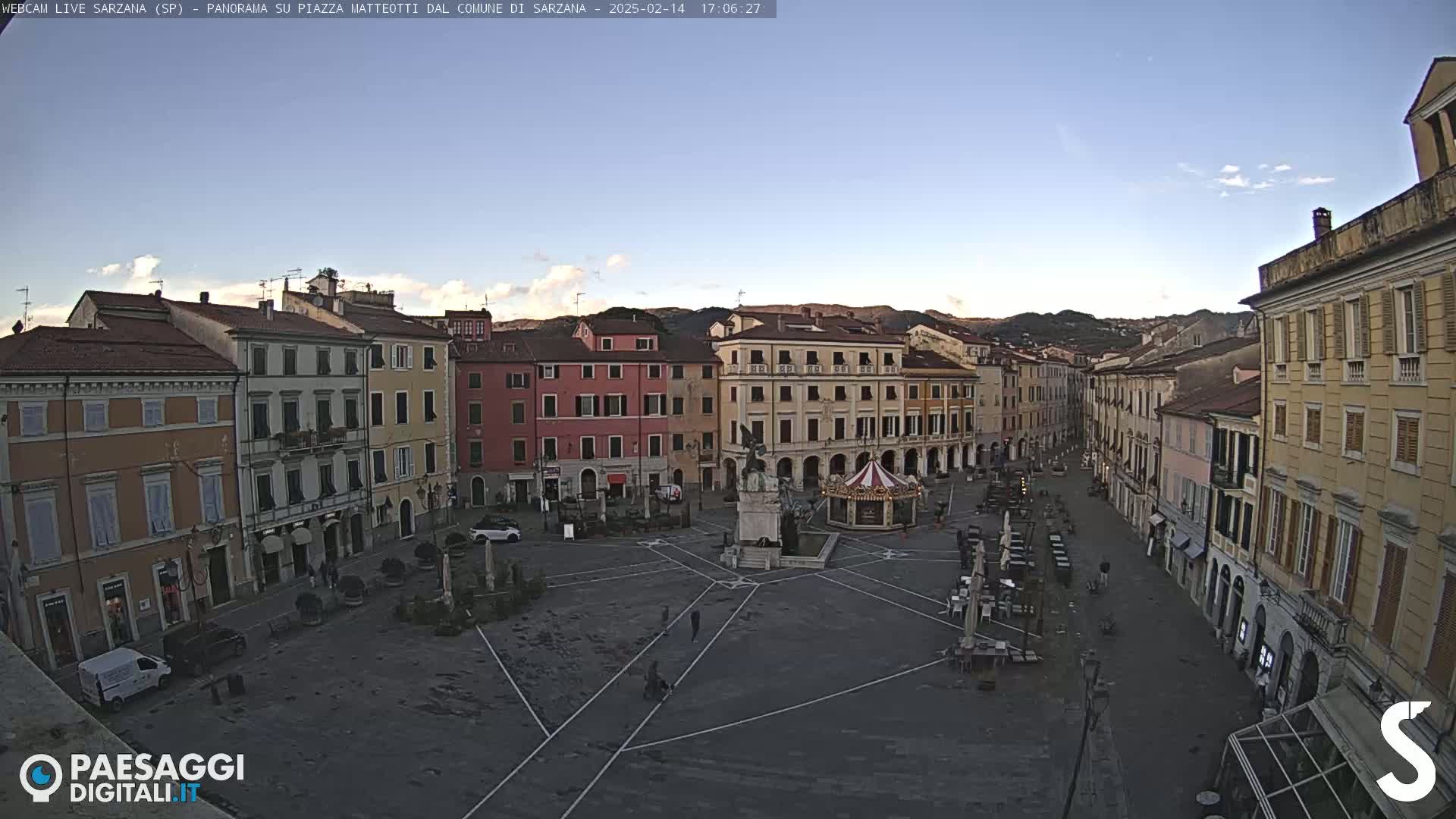 A mostly empty town square, surrounded by multi-story buildings, under a clear, light blue sky.