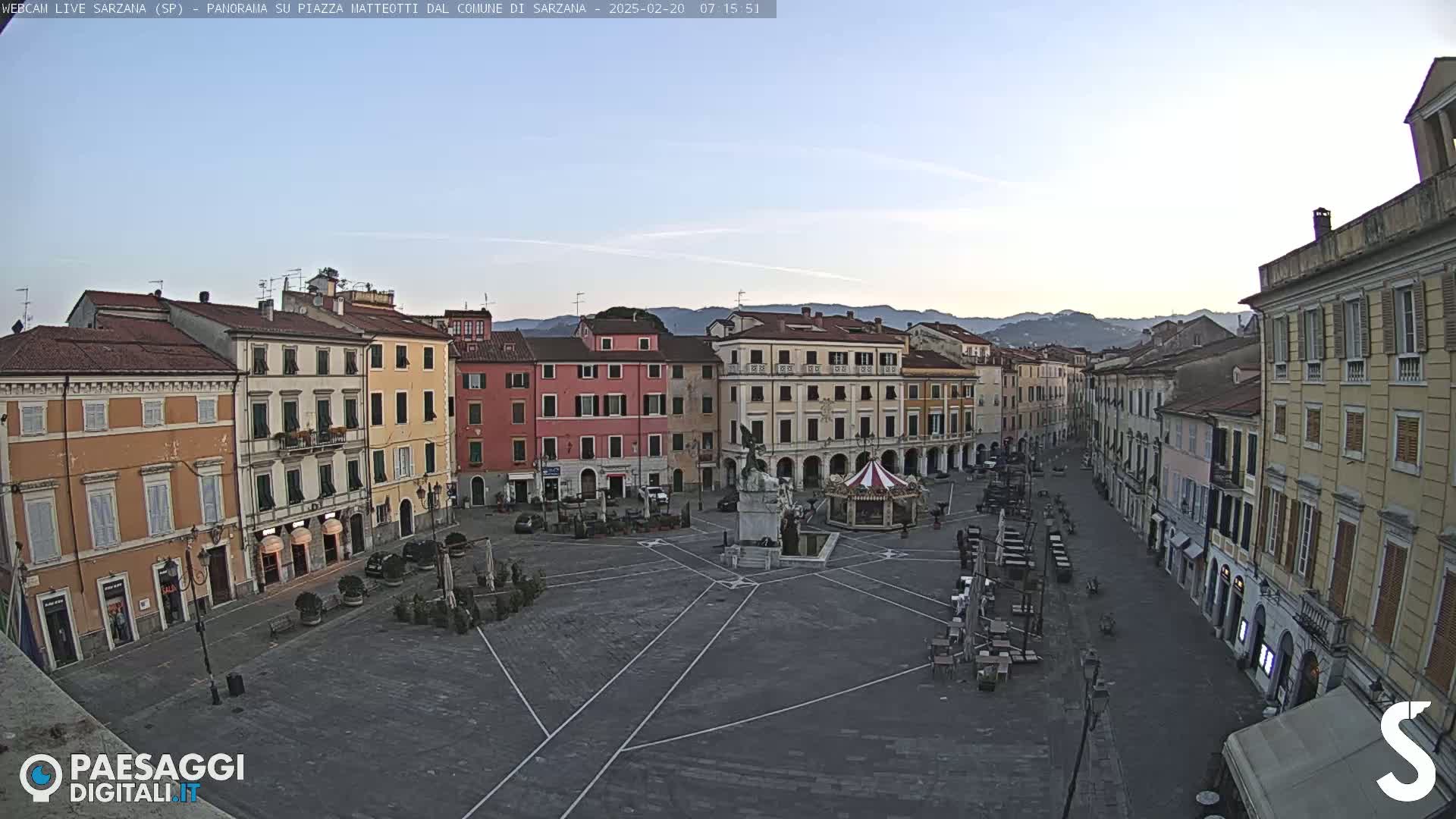 A mostly empty town square with surrounding buildings under a clear, bright sky.
