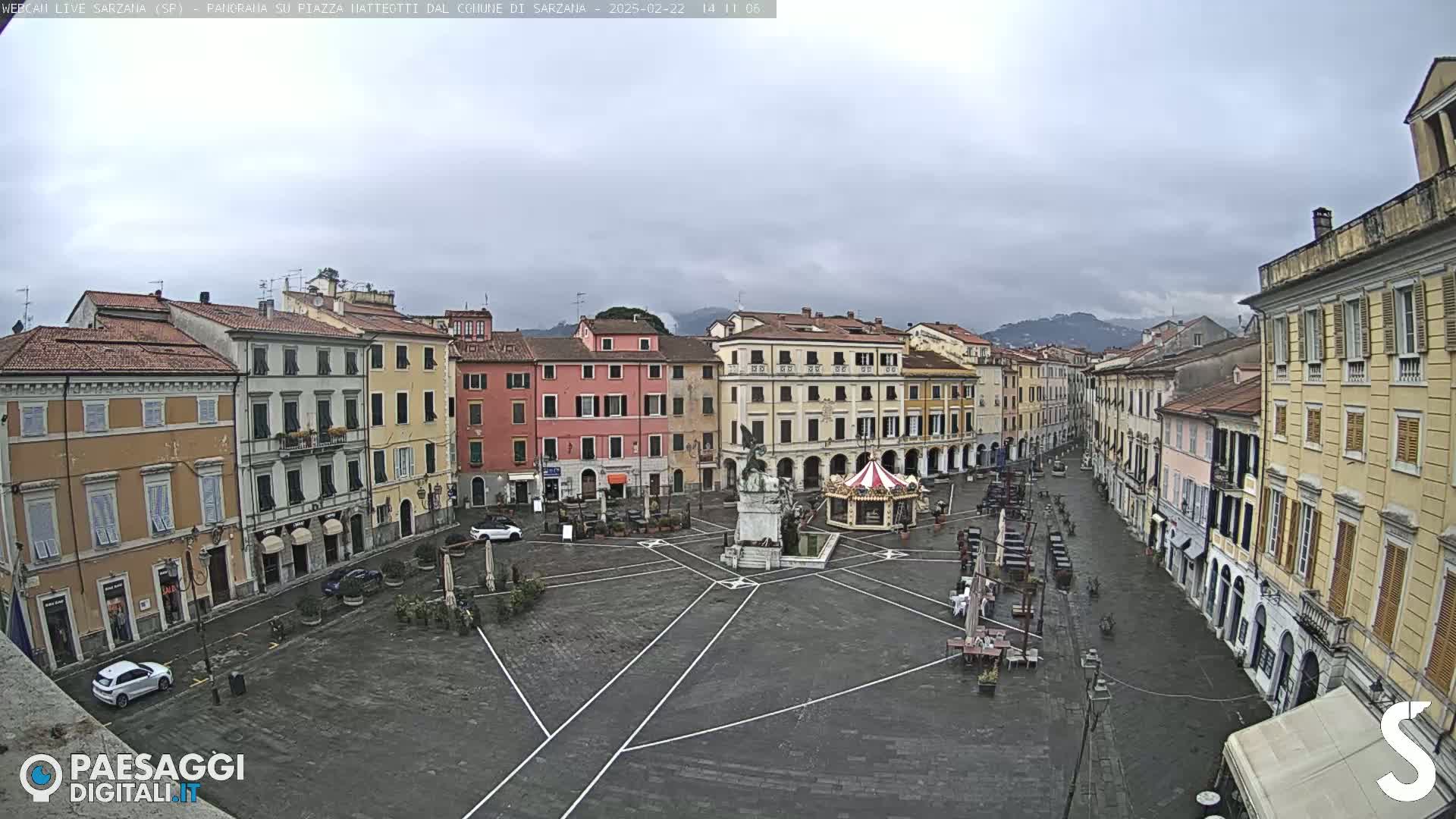 A mostly empty town square with several multi-story buildings surrounding it under an overcast sky.