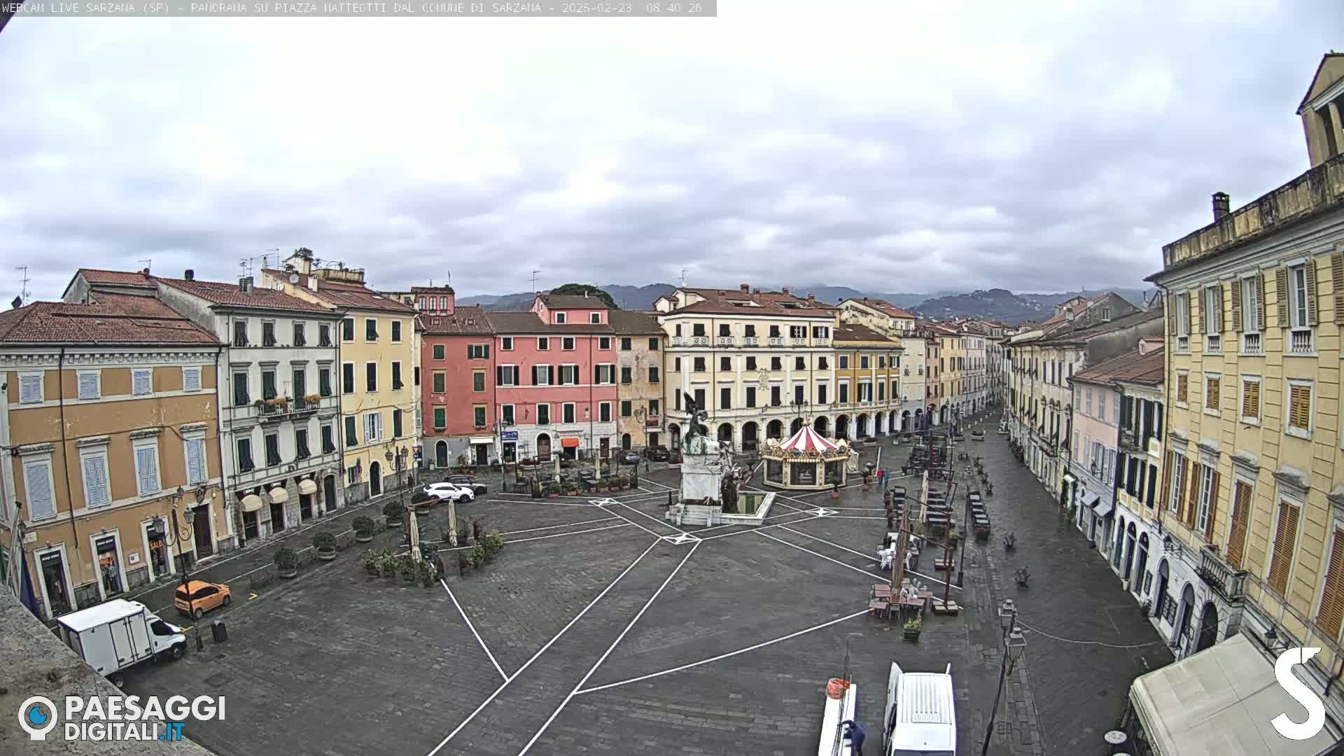A mostly empty town square with several multi-story buildings surrounding it under an overcast sky.