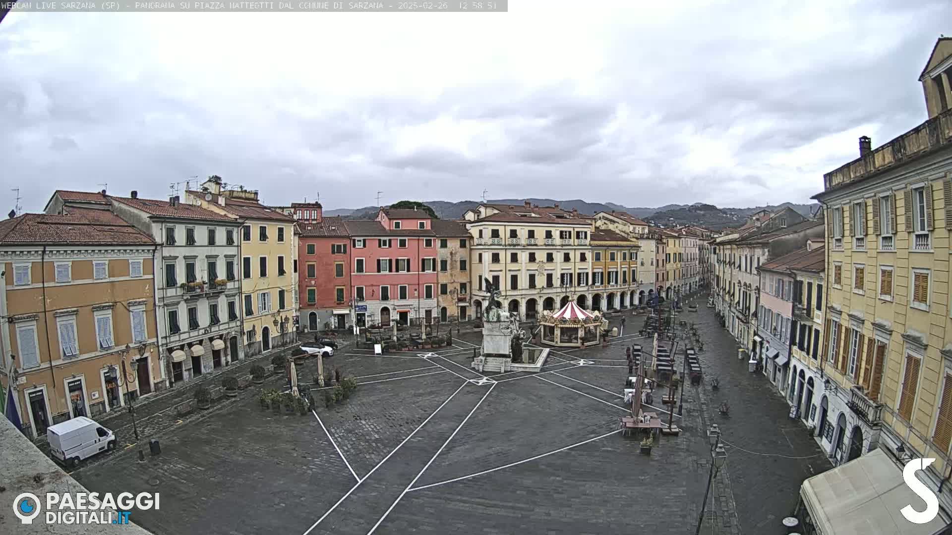 A large, empty town square with surrounding buildings under an overcast sky.