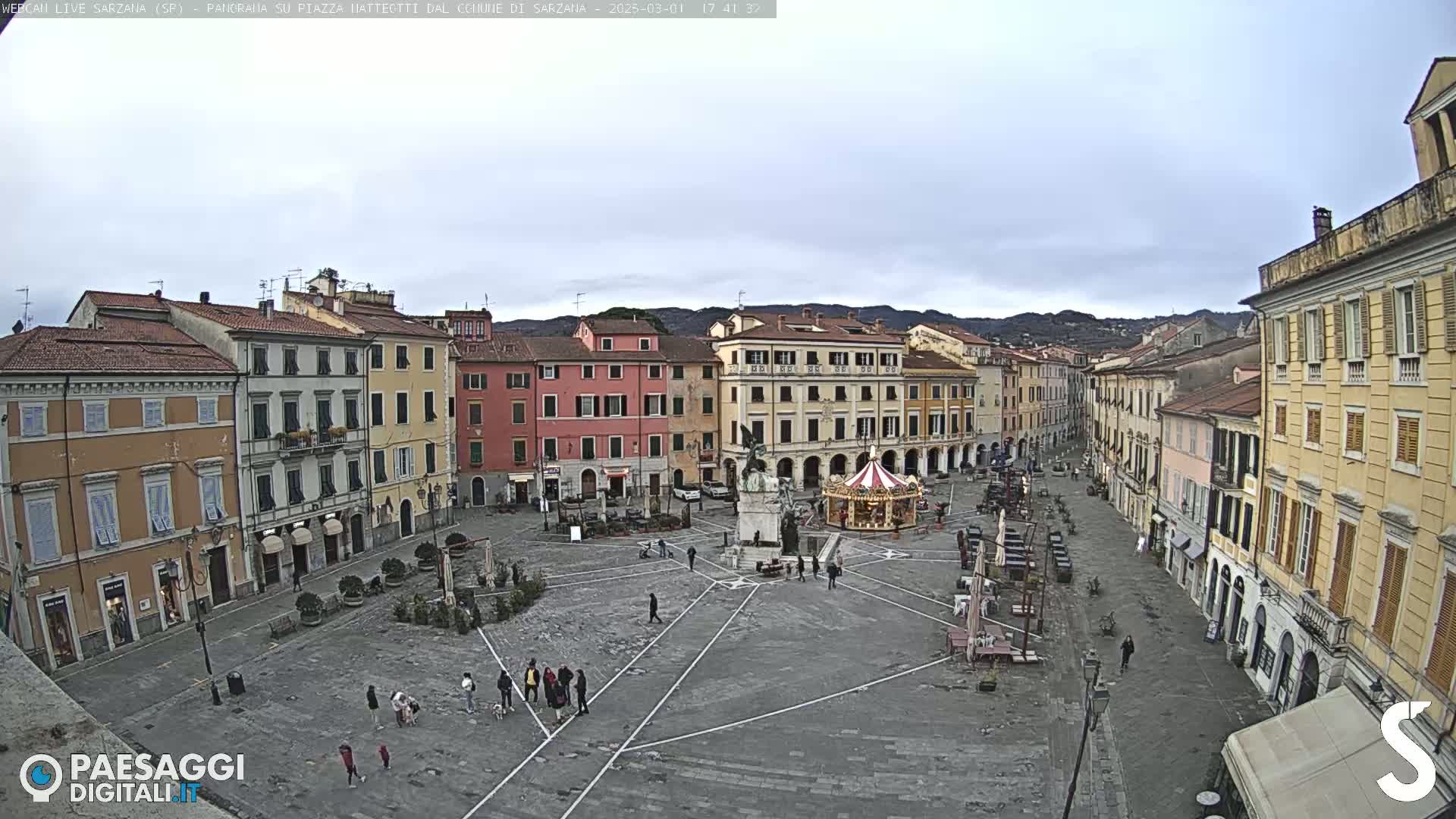 A large, mostly empty town square with several buildings surrounding it under an overcast sky.