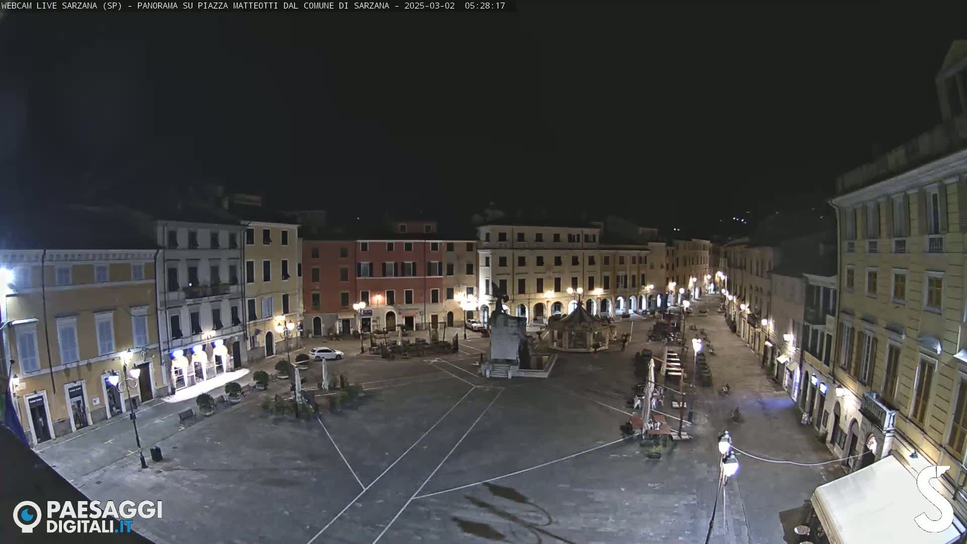 A nighttime, high-angle view of a mostly empty town square surrounded by illuminated buildings.
