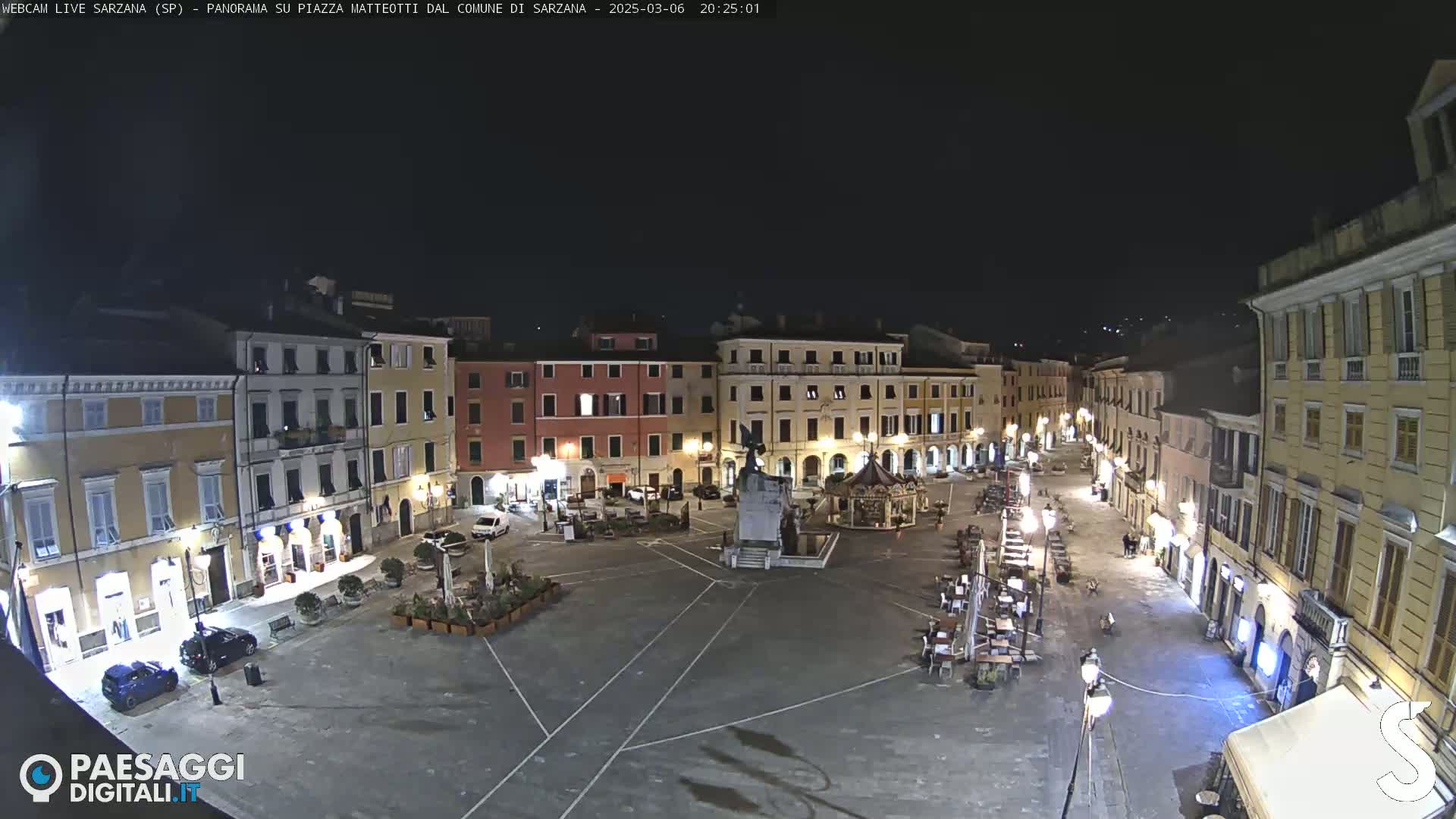 A nighttime view of a town square with several buildings surrounding it, illuminated by streetlights.