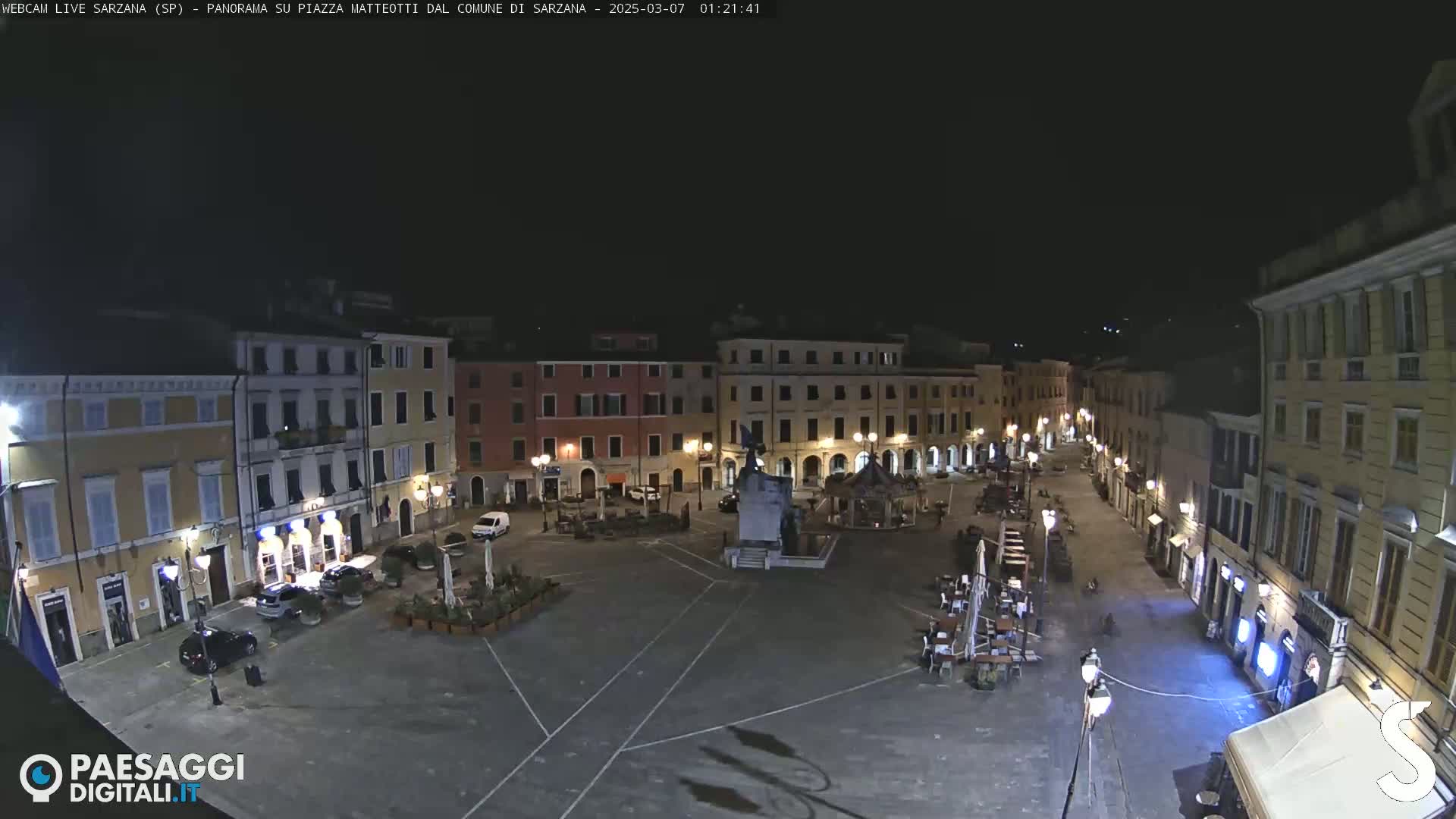 A nighttime, overhead view of a mostly empty town square surrounded by buildings with illuminated windows.