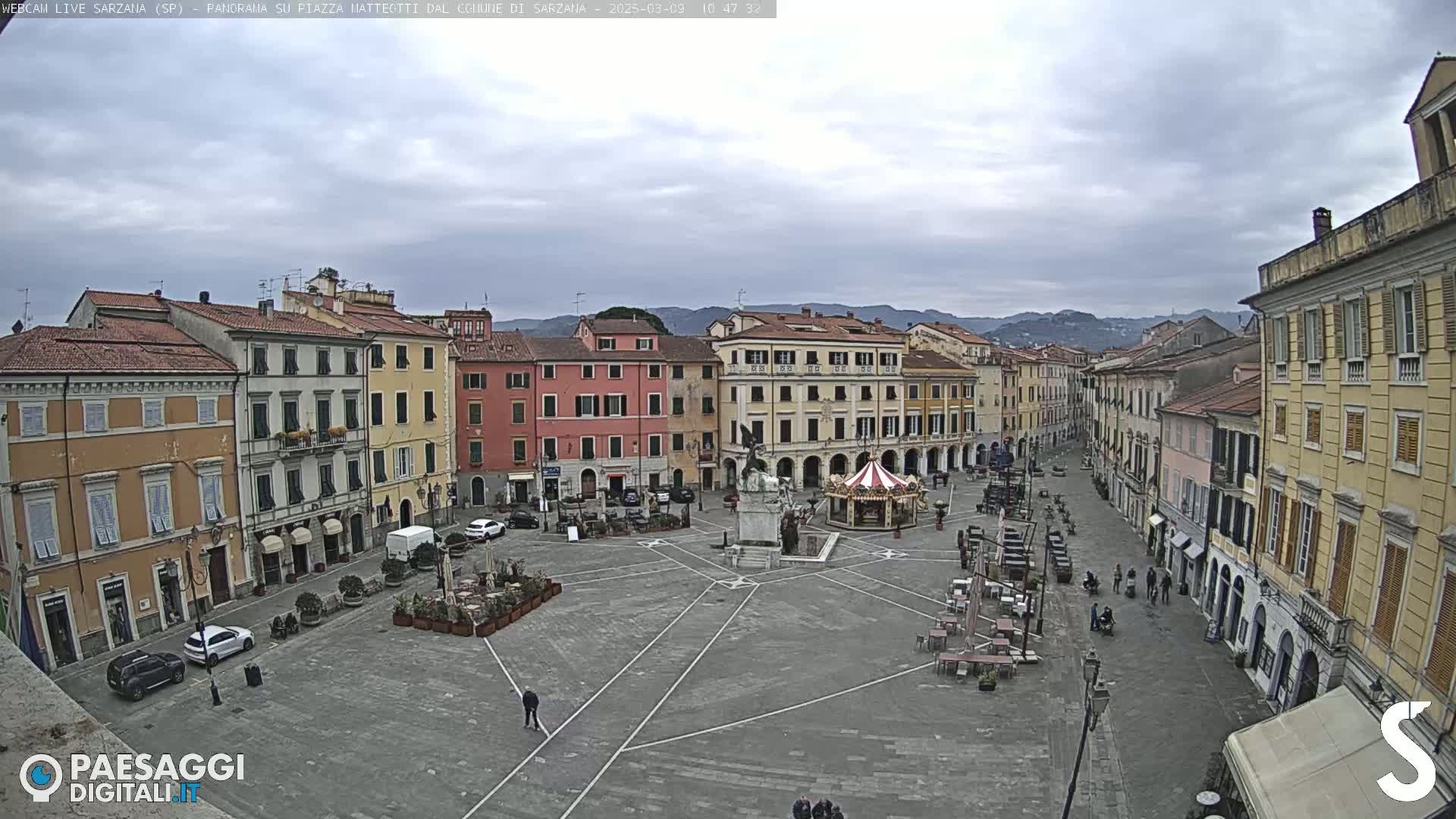 A mostly empty town square with surrounding buildings under an overcast sky.