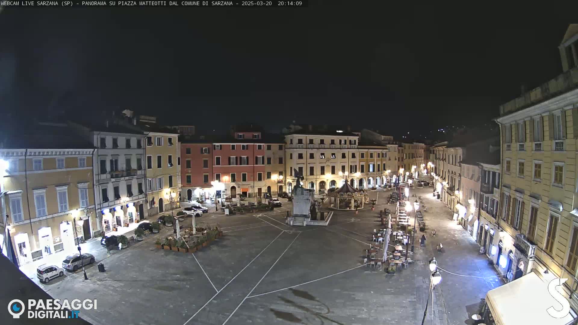 A nighttime, aerial view of a town square with several buildings surrounding it, illuminated by streetlights.
