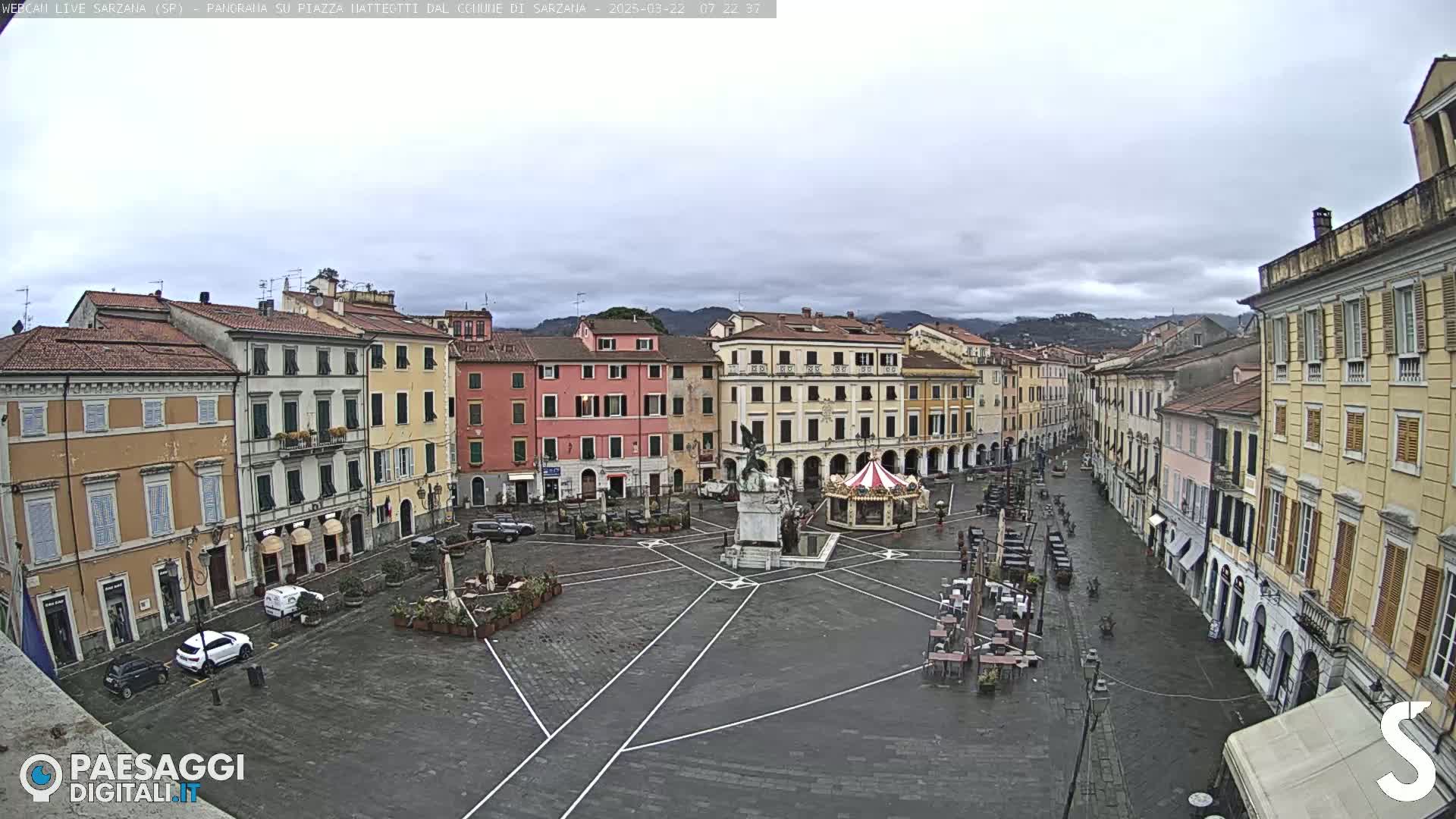 A mostly empty town square, surrounded by multi-story buildings, under an overcast sky.
