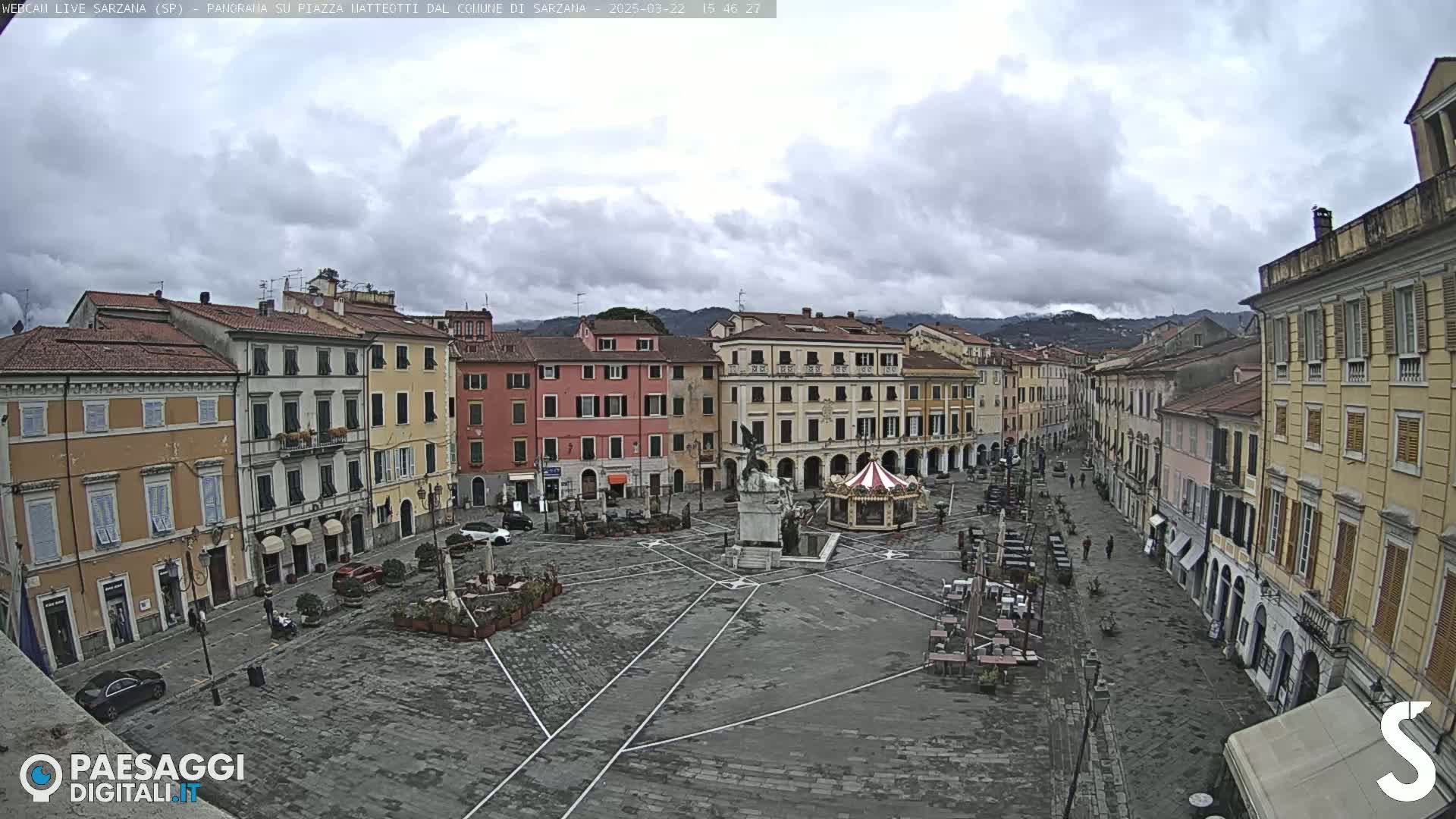 A large town square with several multi-story buildings surrounding it under an overcast sky.