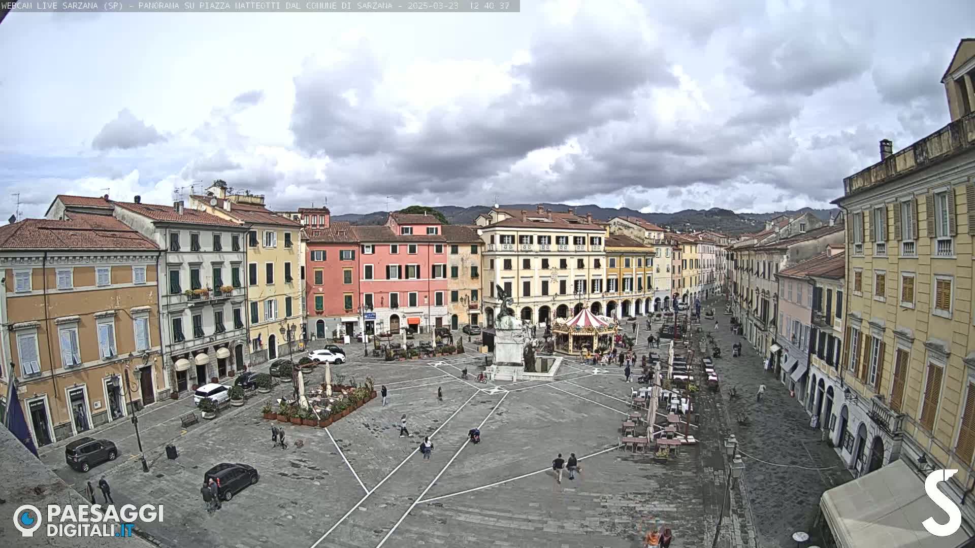 A town square with multi-storied buildings surrounding it under a partly cloudy sky.