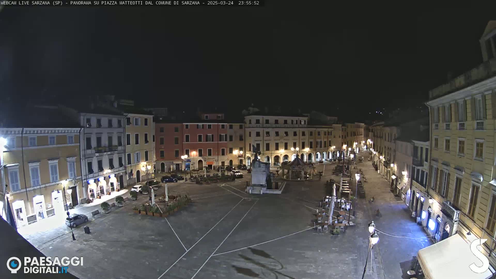 A nighttime, aerial view of a mostly empty town square surrounded by illuminated buildings.