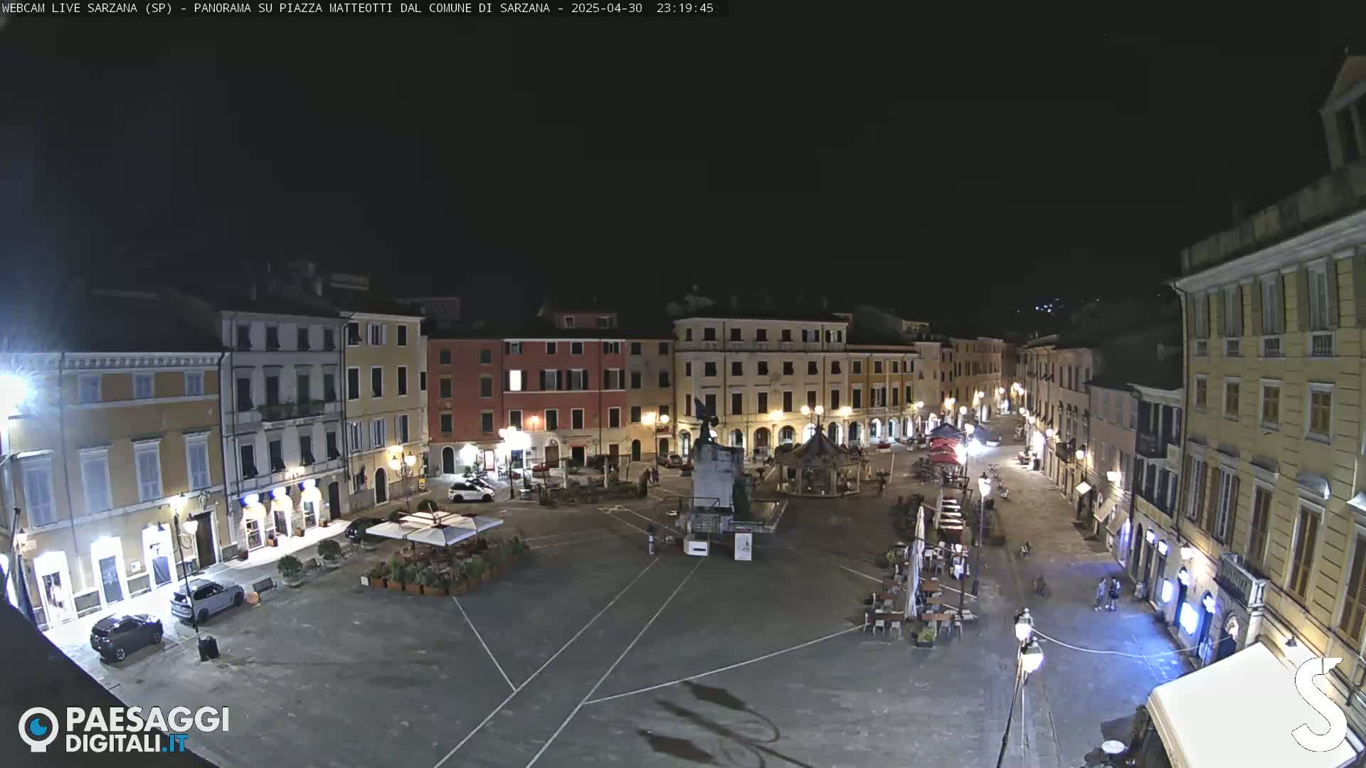 A nighttime, aerial view of a mostly empty town square surrounded by illuminated buildings.