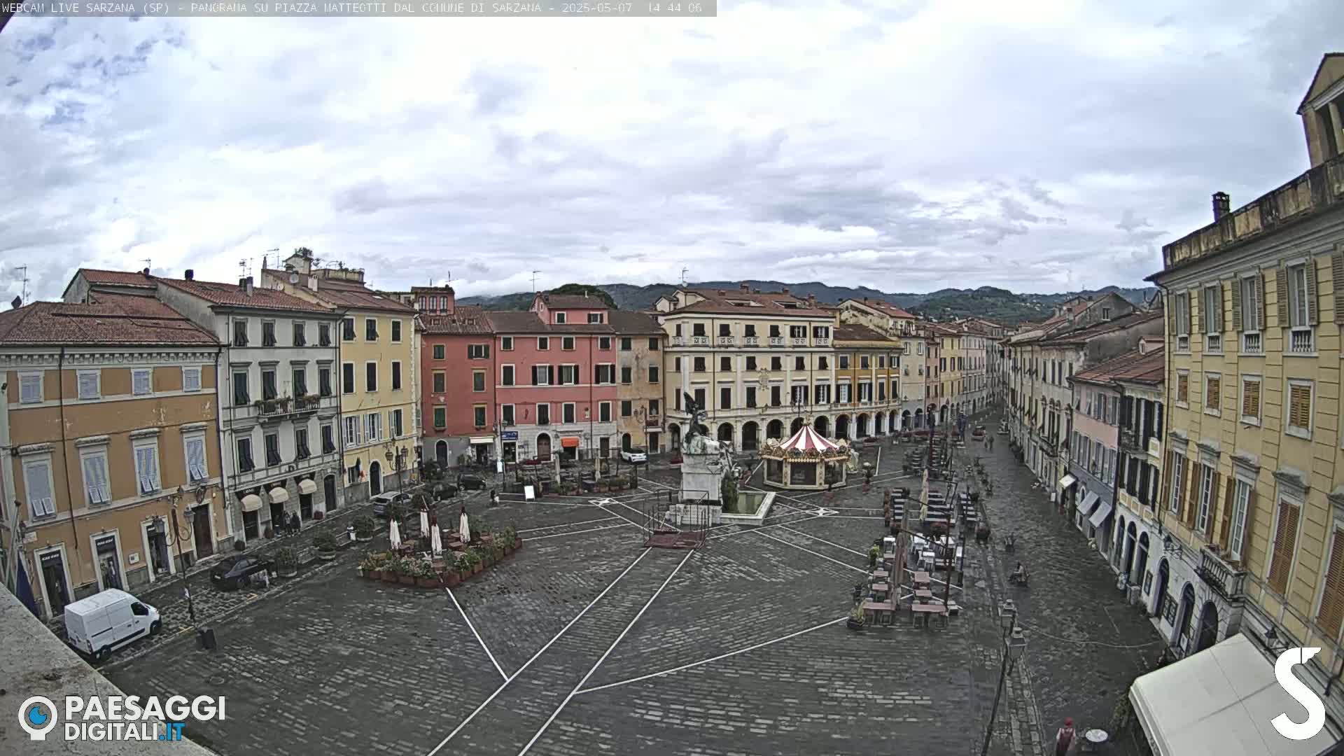 A mostly empty cobblestone town square, surrounded by multi-story buildings, under a cloudy sky.