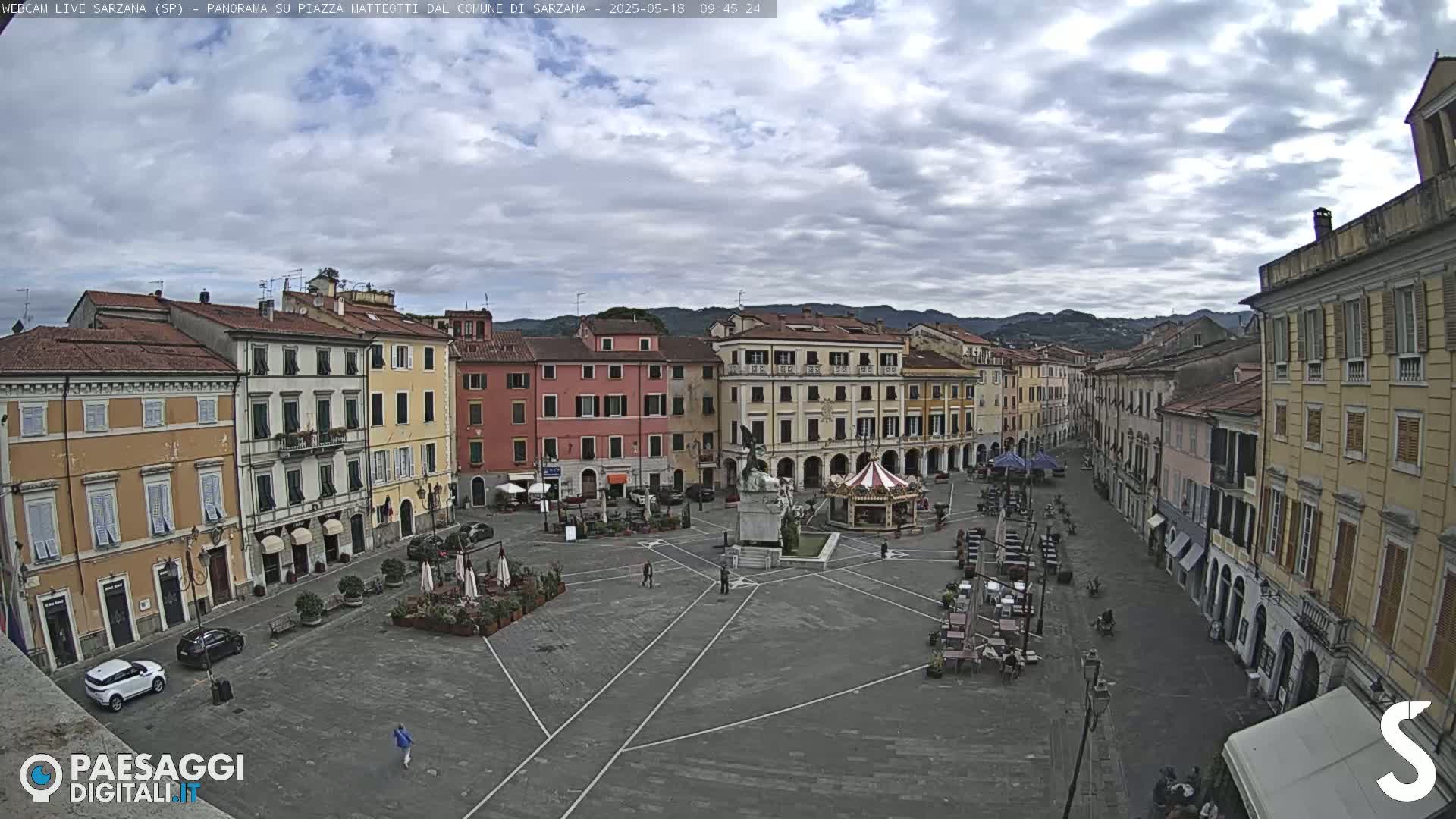 A large, mostly empty town square with several multi-story buildings surrounding it under a cloudy sky.