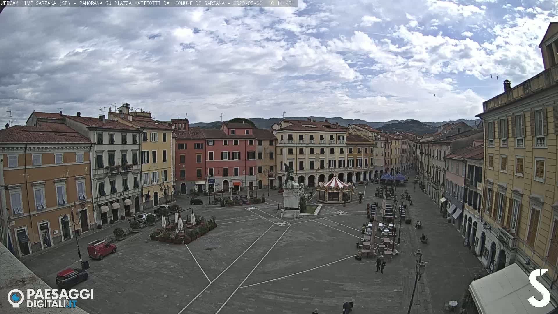 A mostly empty town square, surrounded by multi-story buildings under a partly cloudy sky.