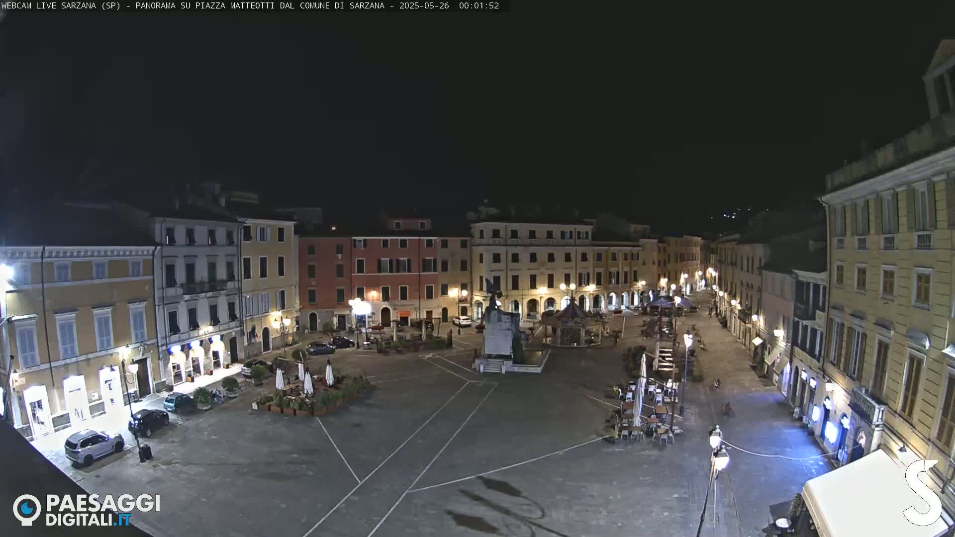 A nighttime, mostly empty town square with surrounding buildings illuminated by streetlights.