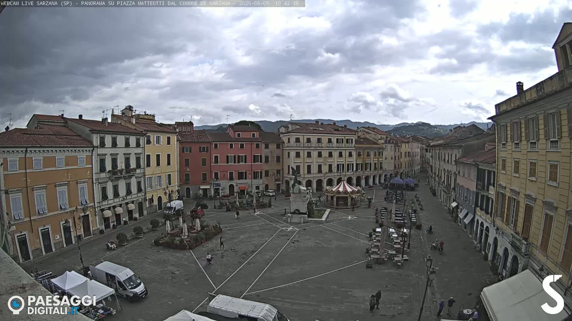 A large, mostly empty town square with multi-story buildings surrounding it under a cloudy sky.