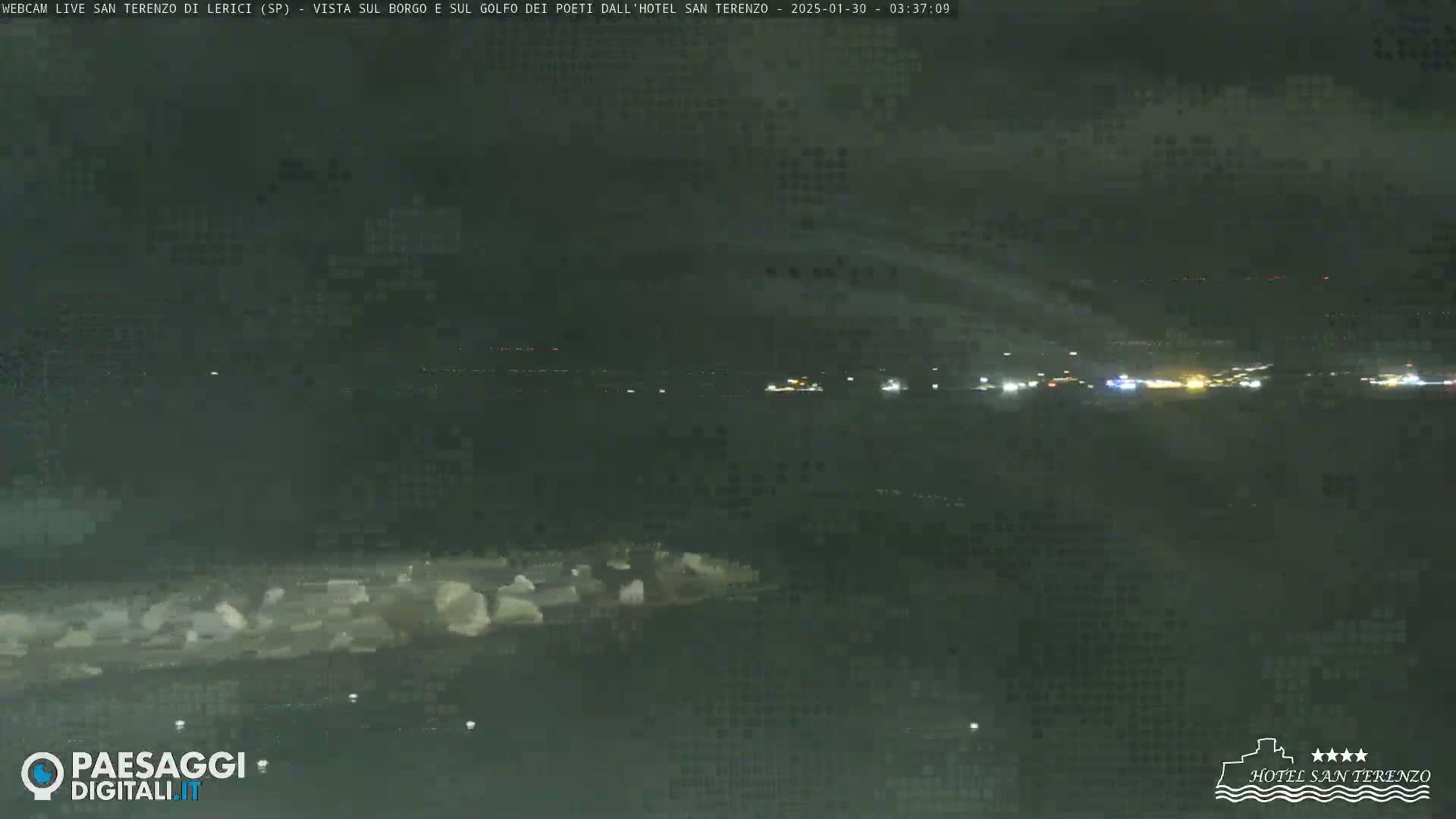 A nighttime long shot shows a dark, hazy coastal area with faint lights visible in the distance.