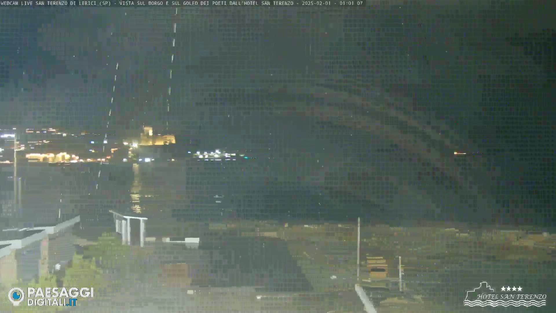 A nighttime view of a city across a body of water, with some light rain or mist in the air.