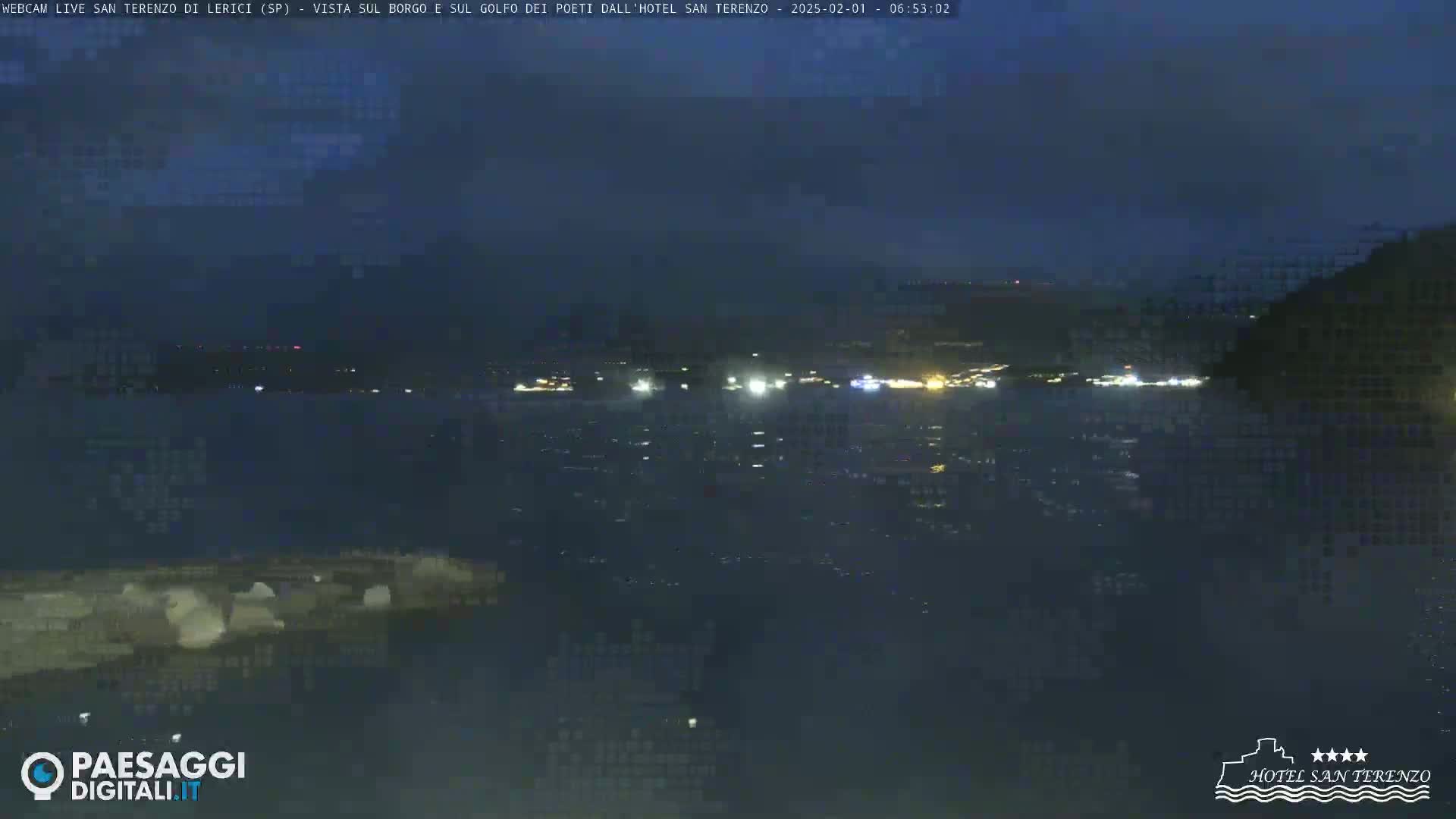 A nighttime view of a dark body of water with a faintly lit town across the water and a dark landmass to the right.