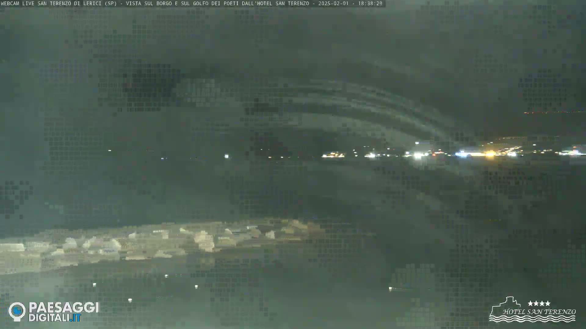 A nighttime view of a coastal town and bay under a cloudy sky.