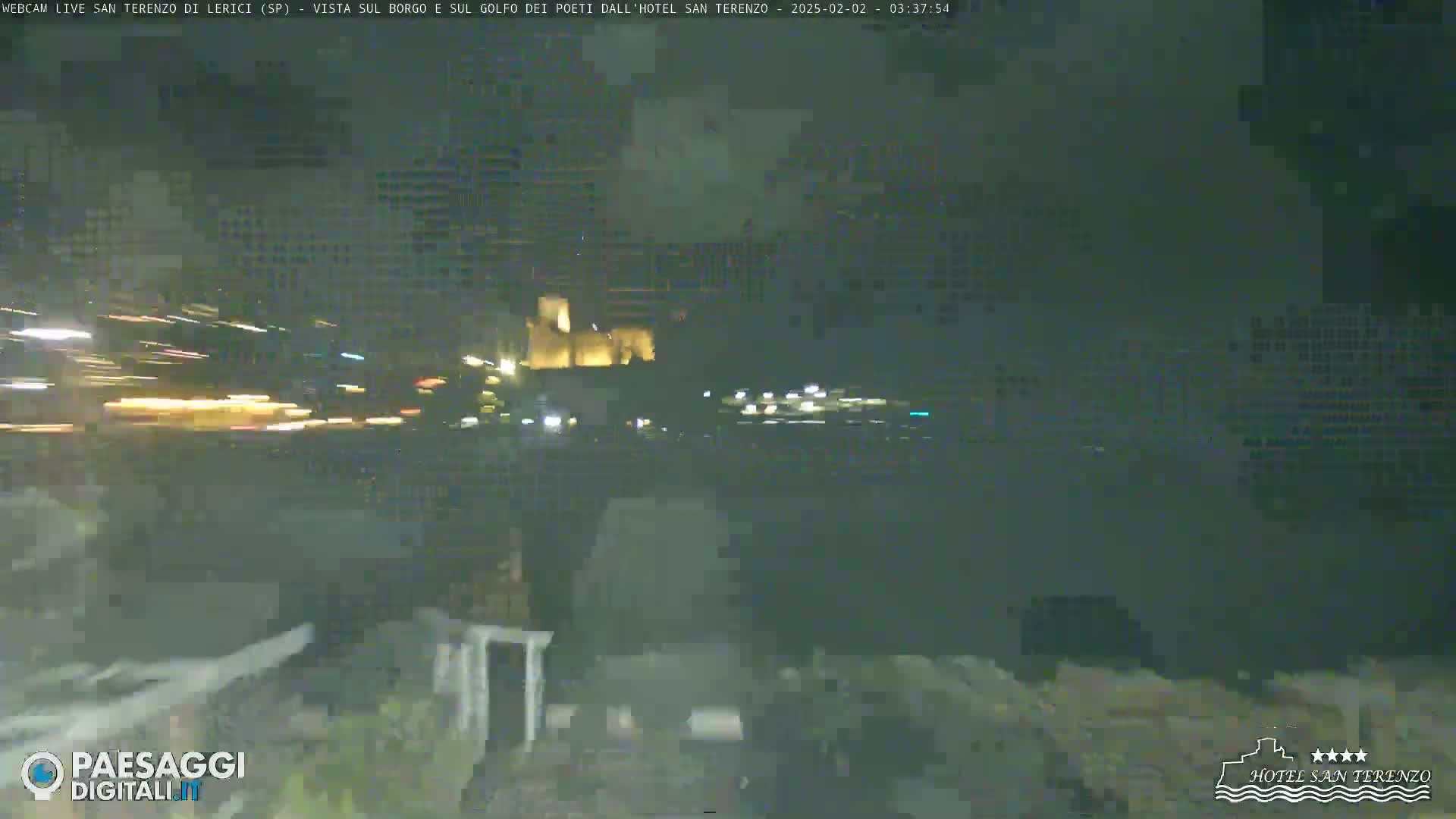 A nighttime view of a town across water, with light trails from vehicles visible in the foreground.