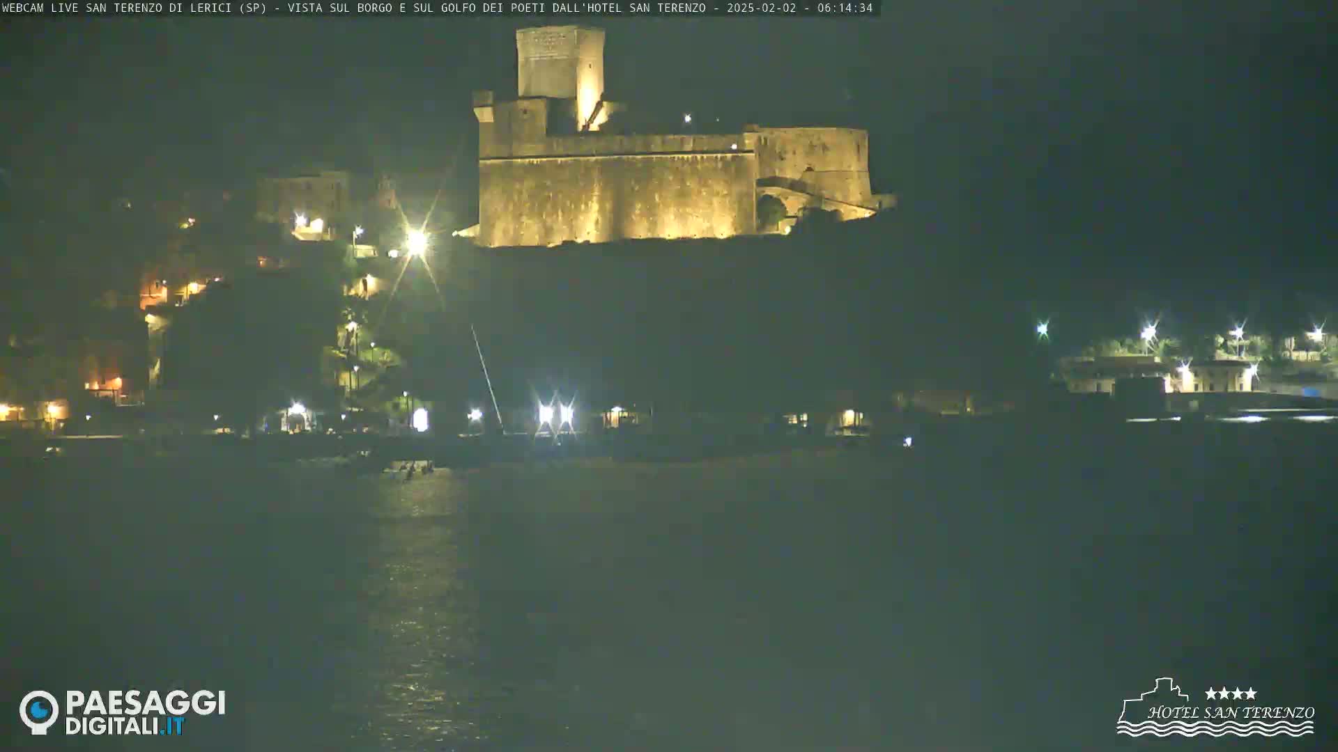 A large stone castle is illuminated at night on a hill overlooking a dark body of water.