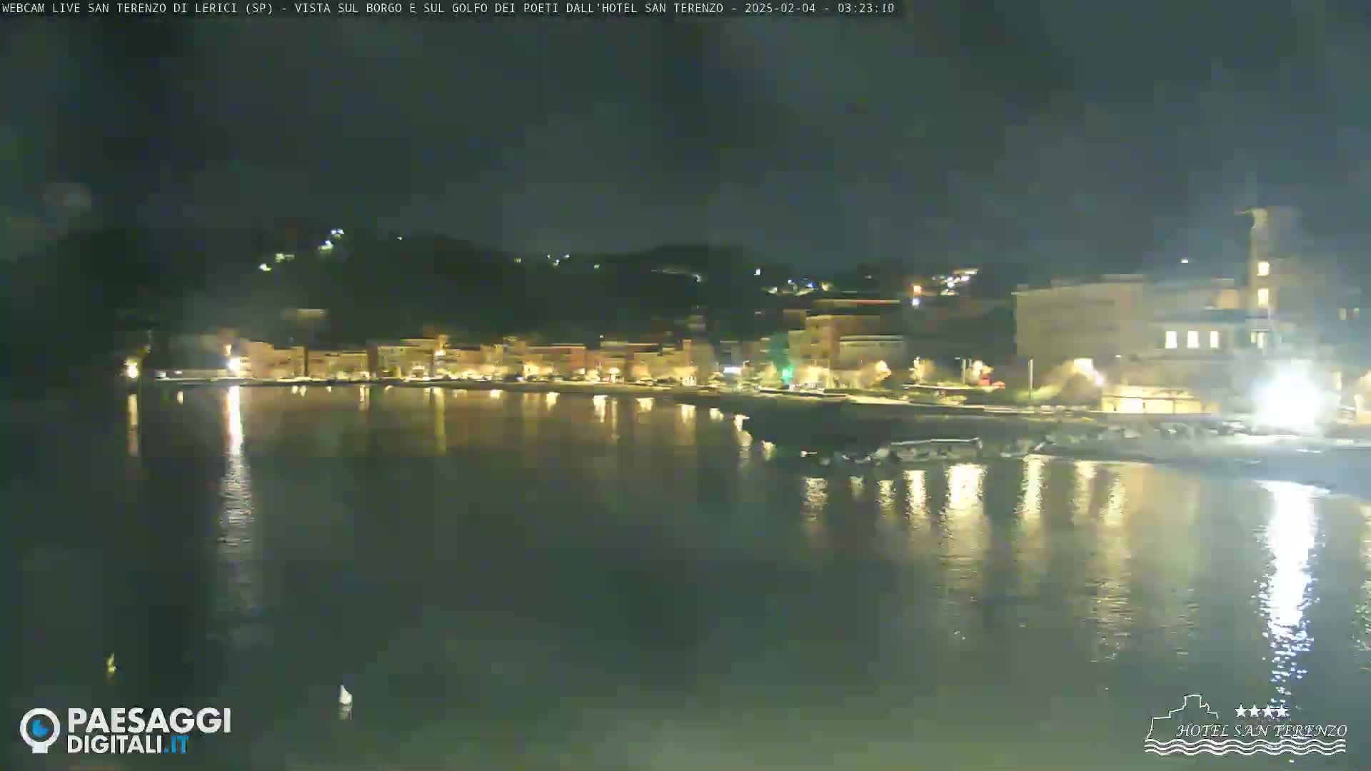 A nighttime view of a calm body of water reflecting the lights of a town nestled against a hillside.
