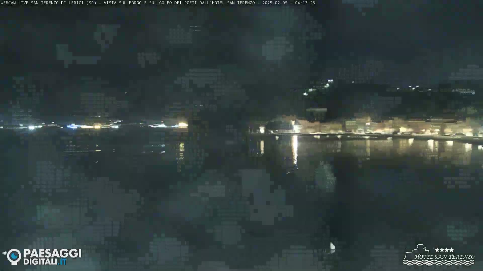 A nighttime view of a calm body of water reflecting the lights of a town on the opposite shore.