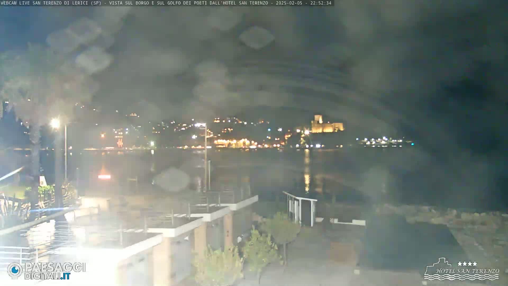 A nighttime view of a town across a body of water, slightly obscured by rain or mist.