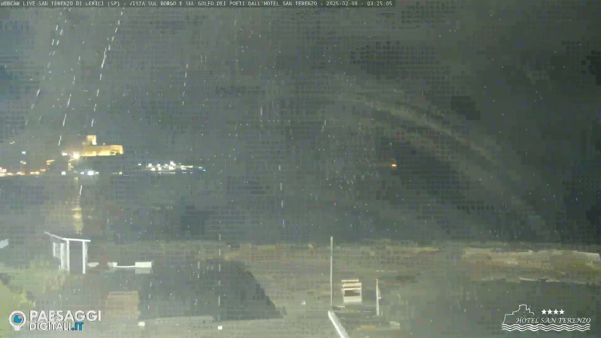 A nighttime view of a town across a body of water during a light rain.