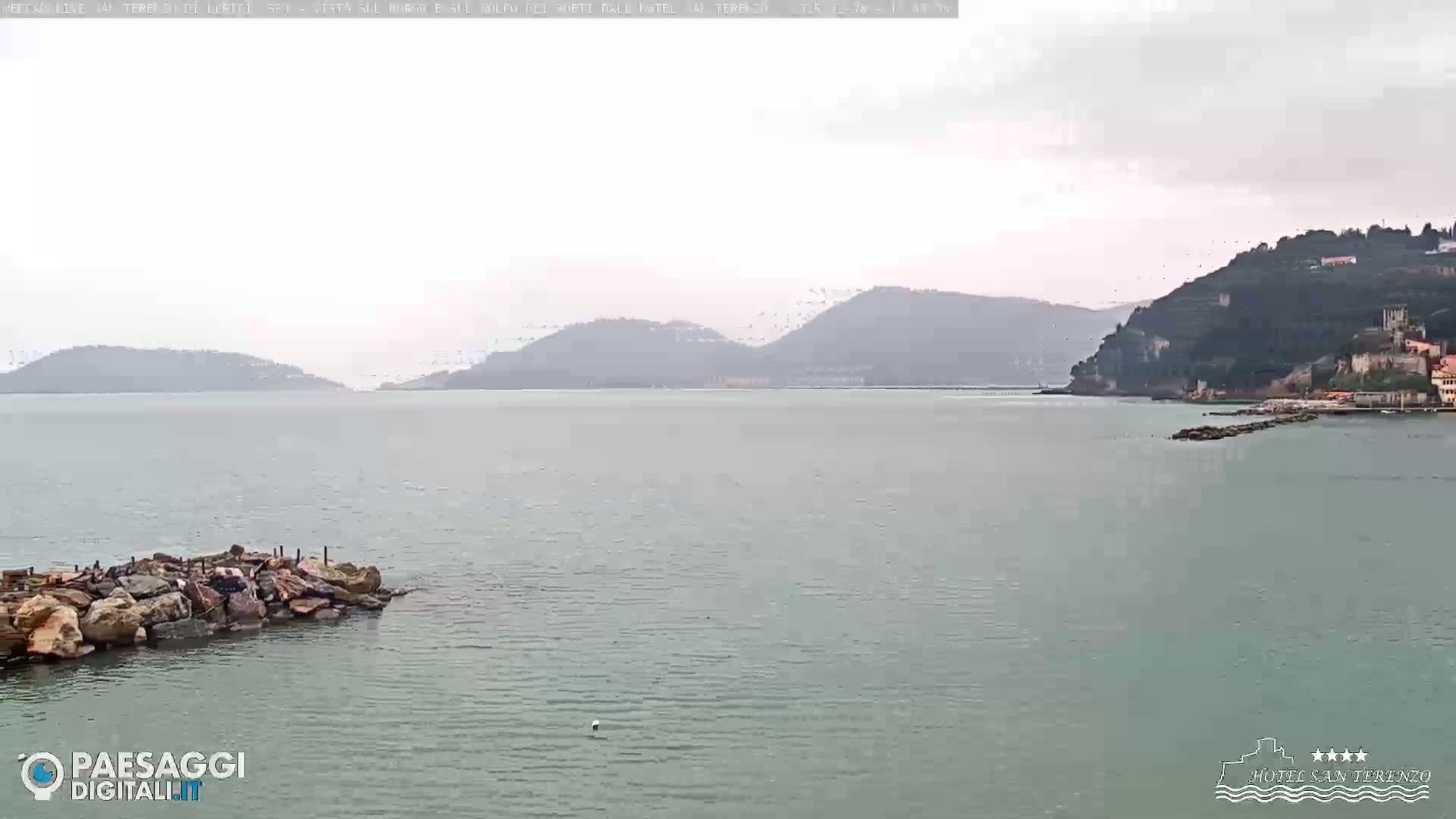 A calm, overcast day shows a body of water with rocky shorelines and hills in the distance.