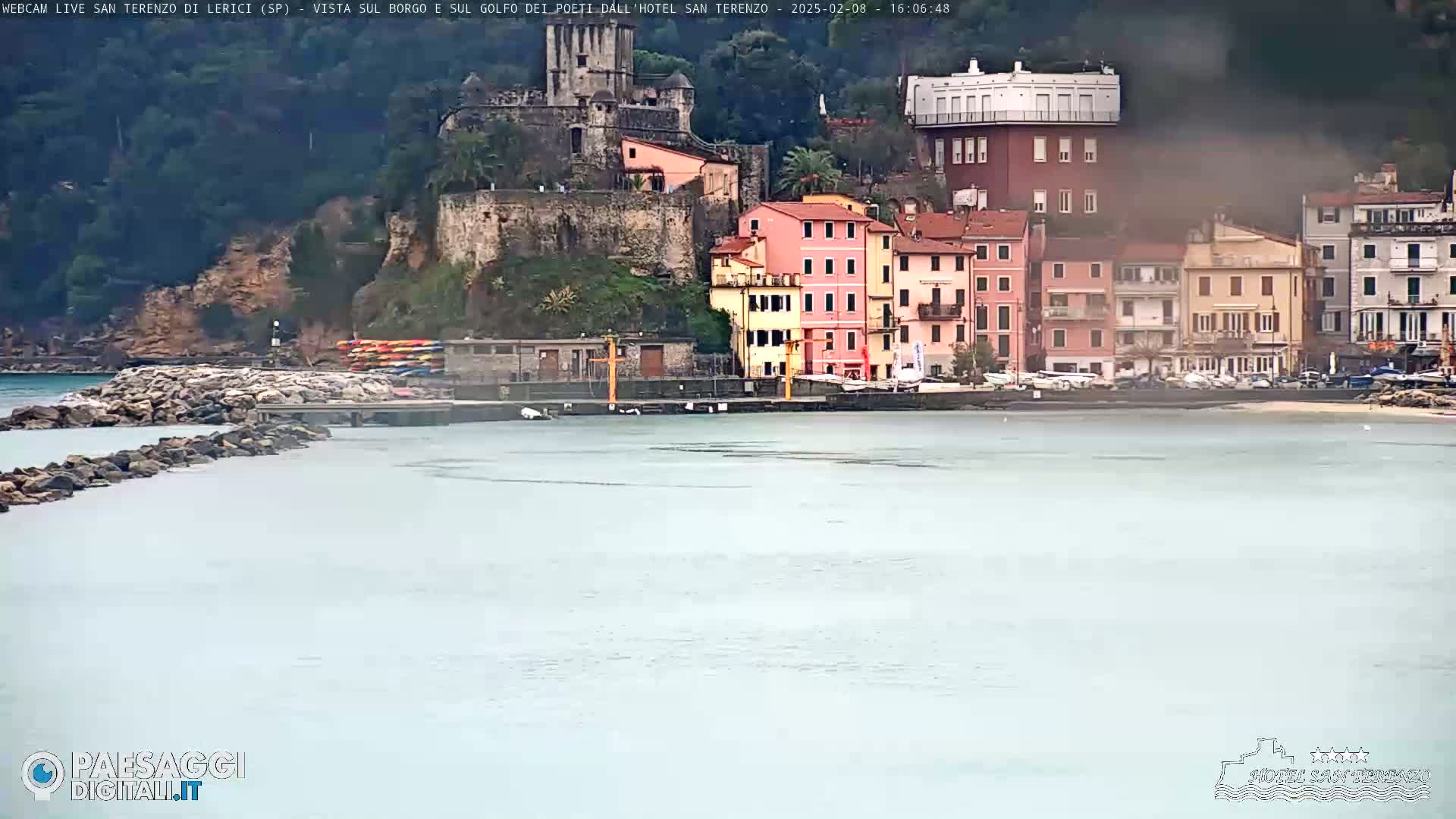 A hazy view of a coastal town with colorful buildings, a stone fortress, and a calm, light-grey sea.