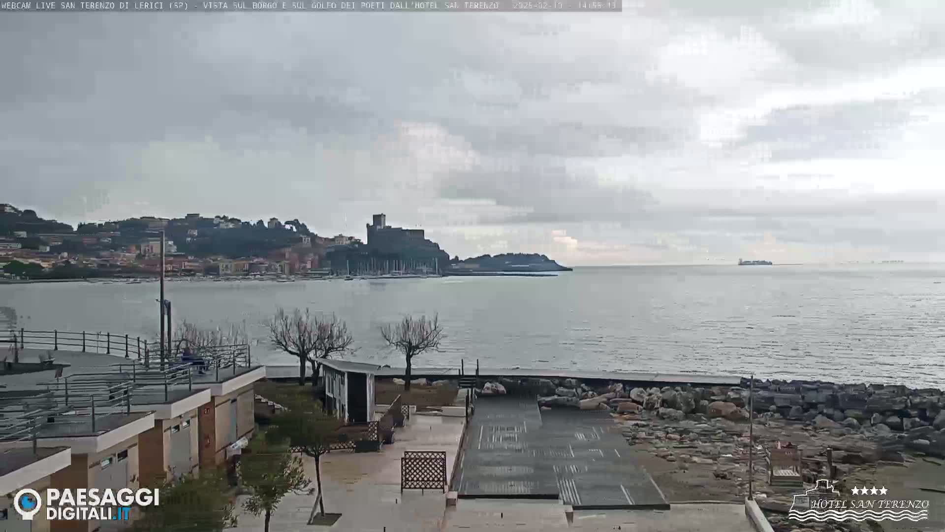 A seaside town with a castle is visible across a calm, gray-water bay on an overcast day.