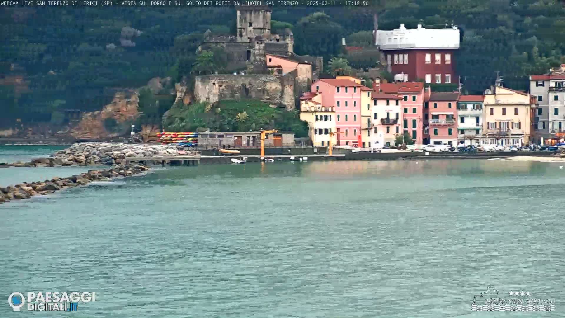 A waterfront town with colorful buildings, a stone breakwater, and calm, slightly choppy water is visible in the overcast weather.
