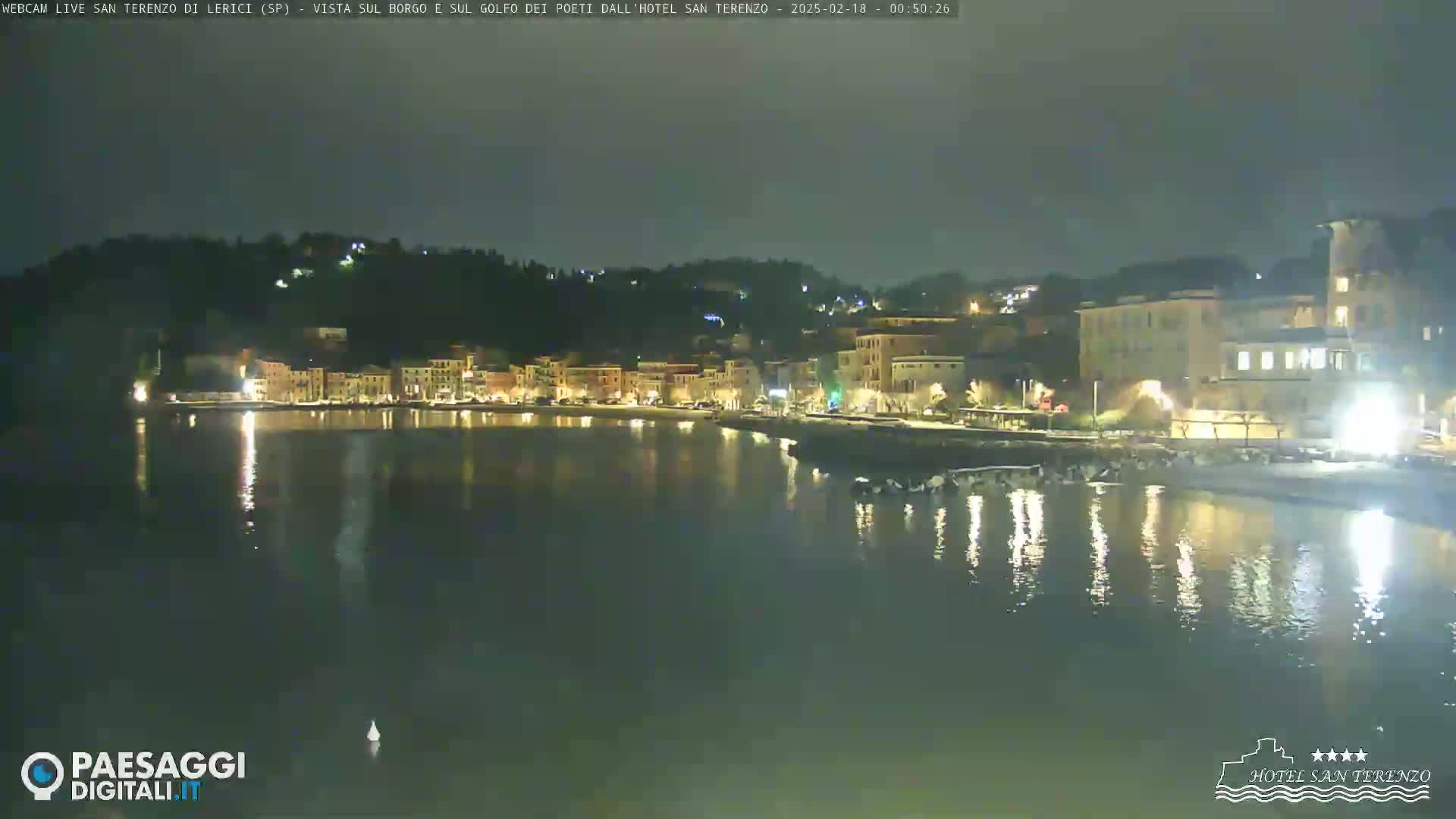A nighttime view of a waterfront town with brightly lit buildings and calm water reflecting the lights.