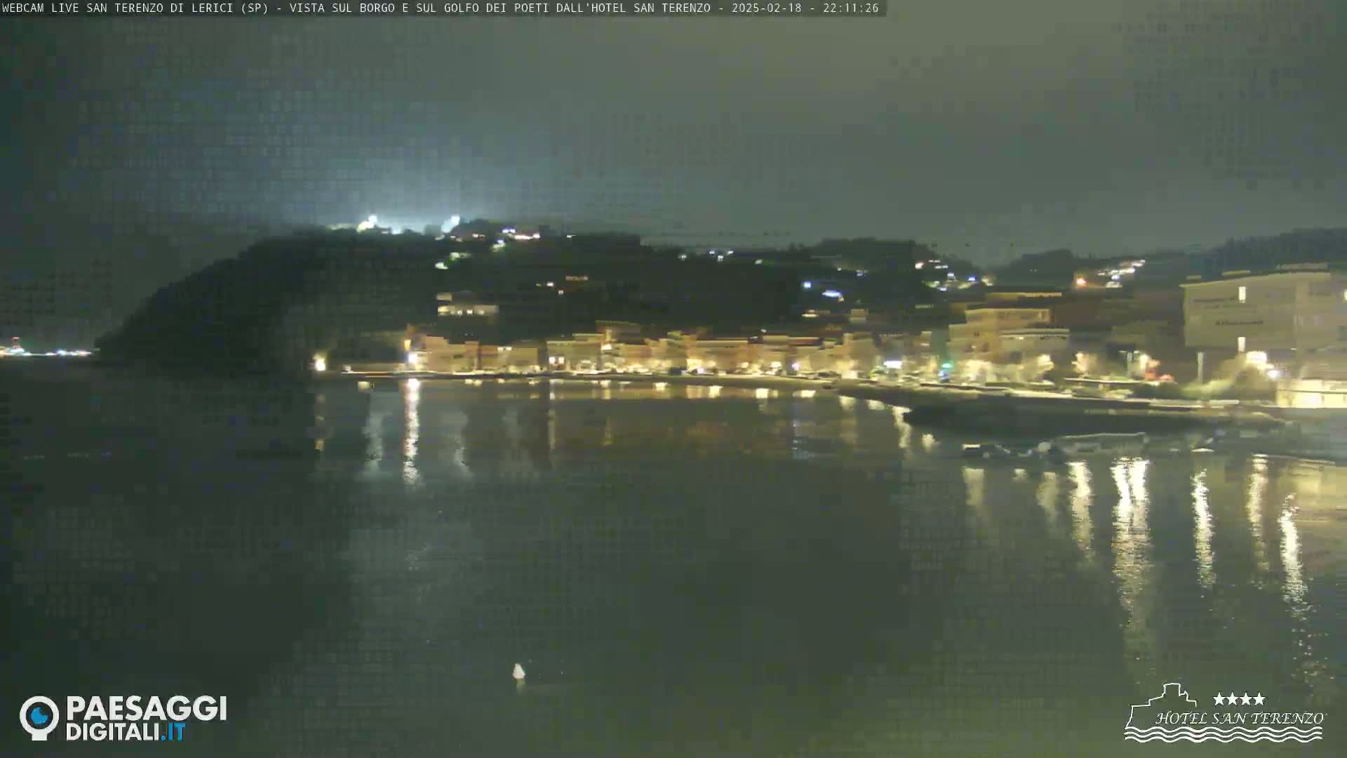 A nighttime view of a town's waterfront, illuminated by lights reflecting on calm water.