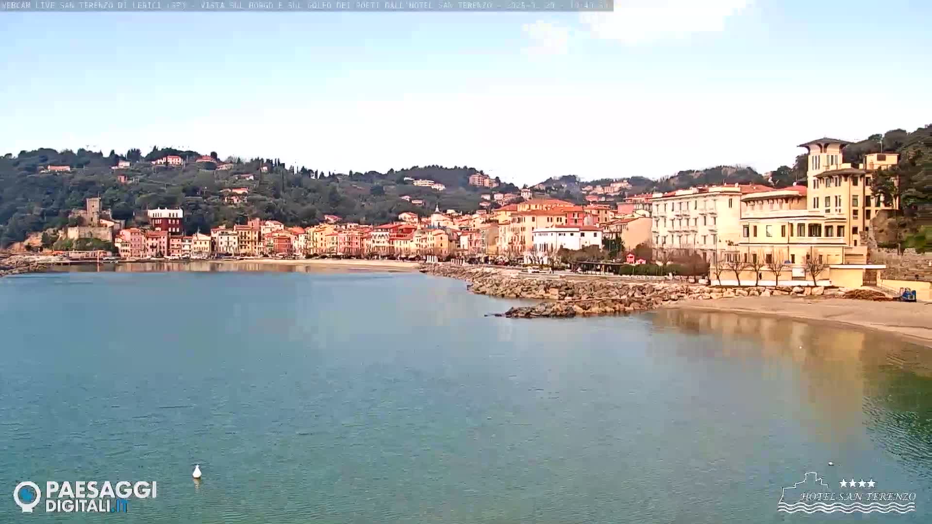 A picturesque coastal town with colorful buildings sits on a hillside overlooking a calm bay under a clear sky.