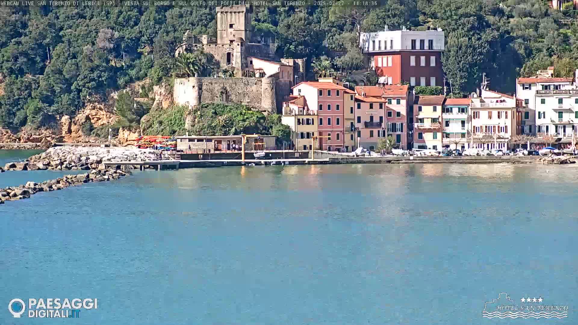 A picturesque coastal town with colorful buildings, a stone jetty, and calm blue water under a sunny sky.
