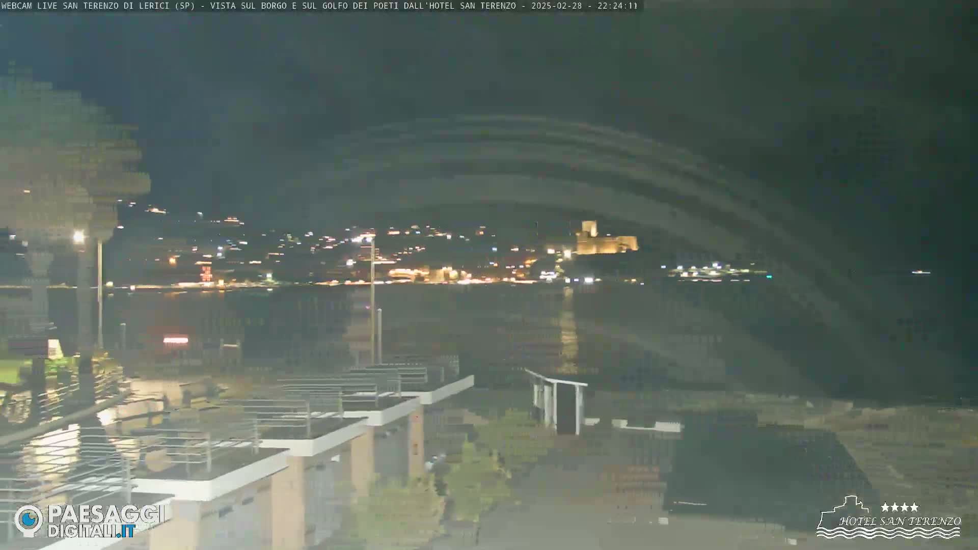 A nighttime view of a town across a body of water, with lights visible in the distance and some structures in the foreground.