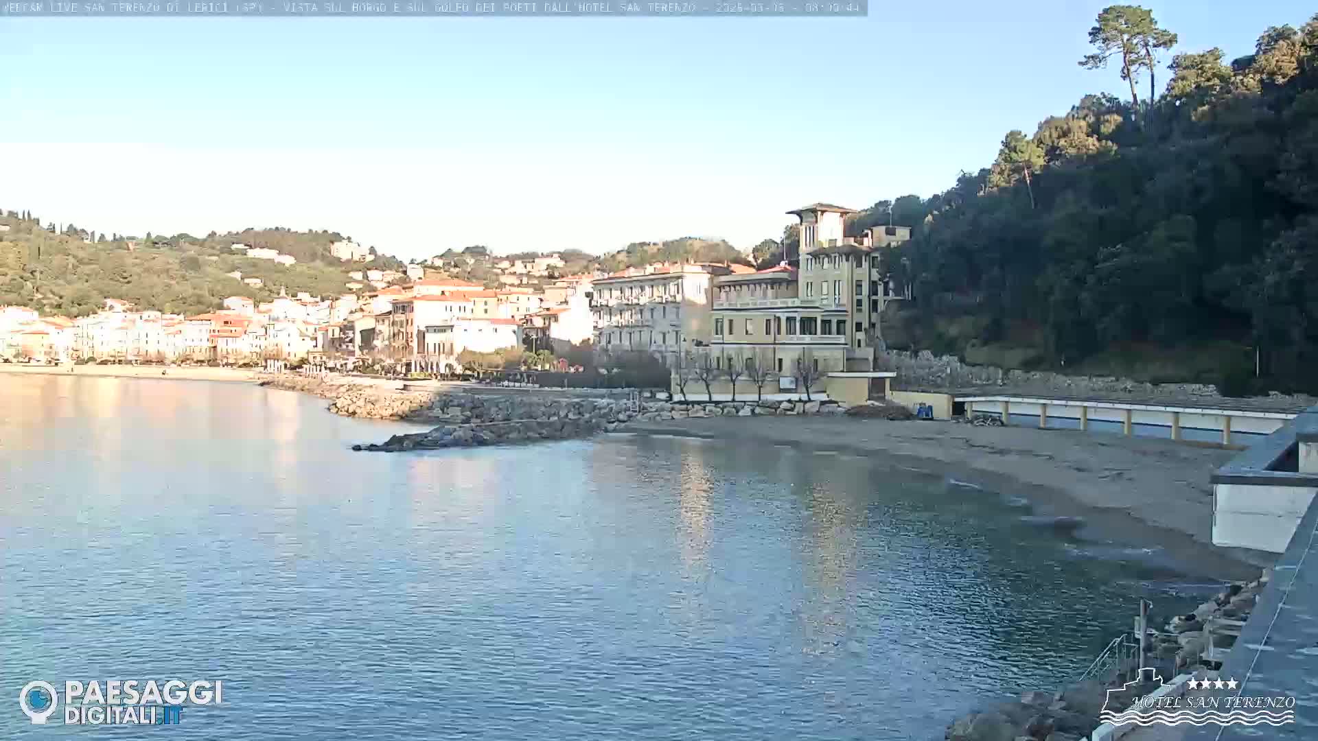 A seaside town with a large building and sandy beach is visible under a clear, sunny sky.