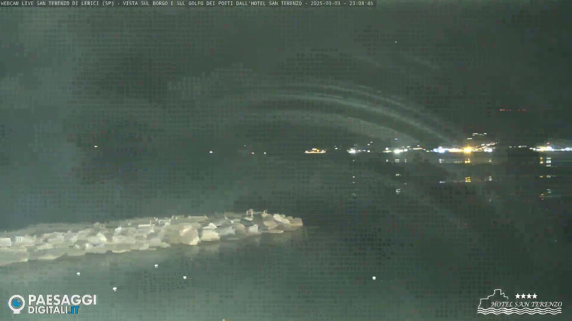 A nighttime long shot shows a body of water with lights visible across it and a collection of lights on the left shore, under a dark, clear sky.